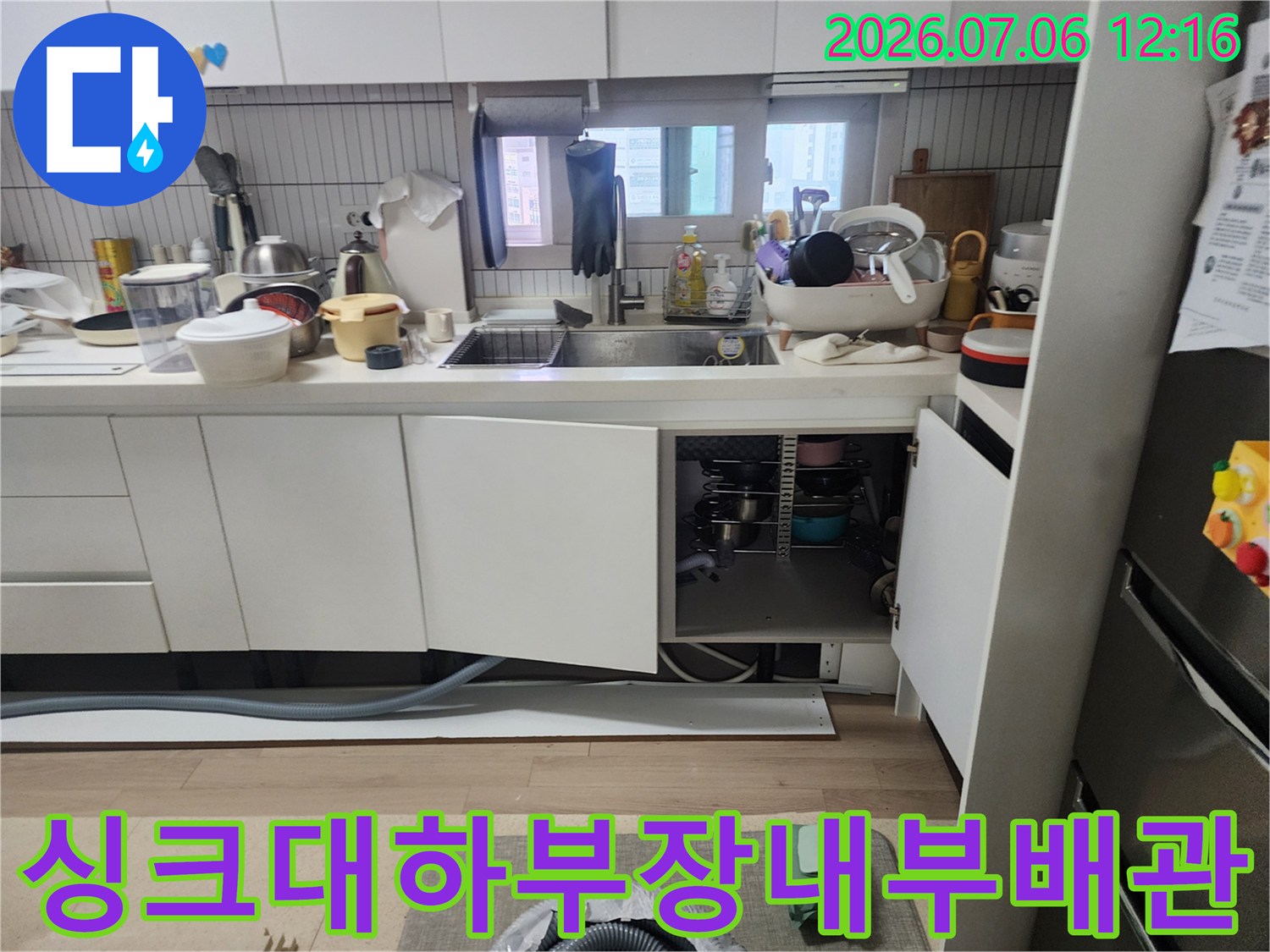 주방 가구 밑 공간에서 배수 시스템과 연결 상태를 점검하는 장면