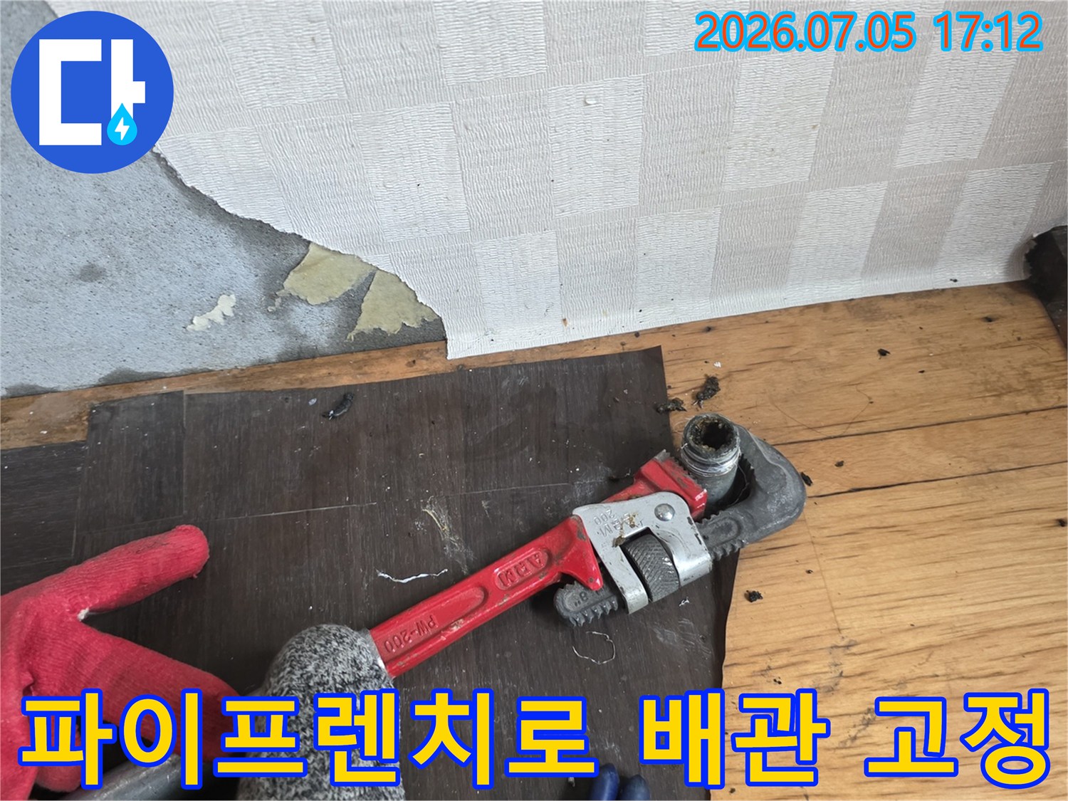 빨간색 파이프렌치를 사용하여 노출된 배관 연결 부위를 단단히 조이는 작업 모습
