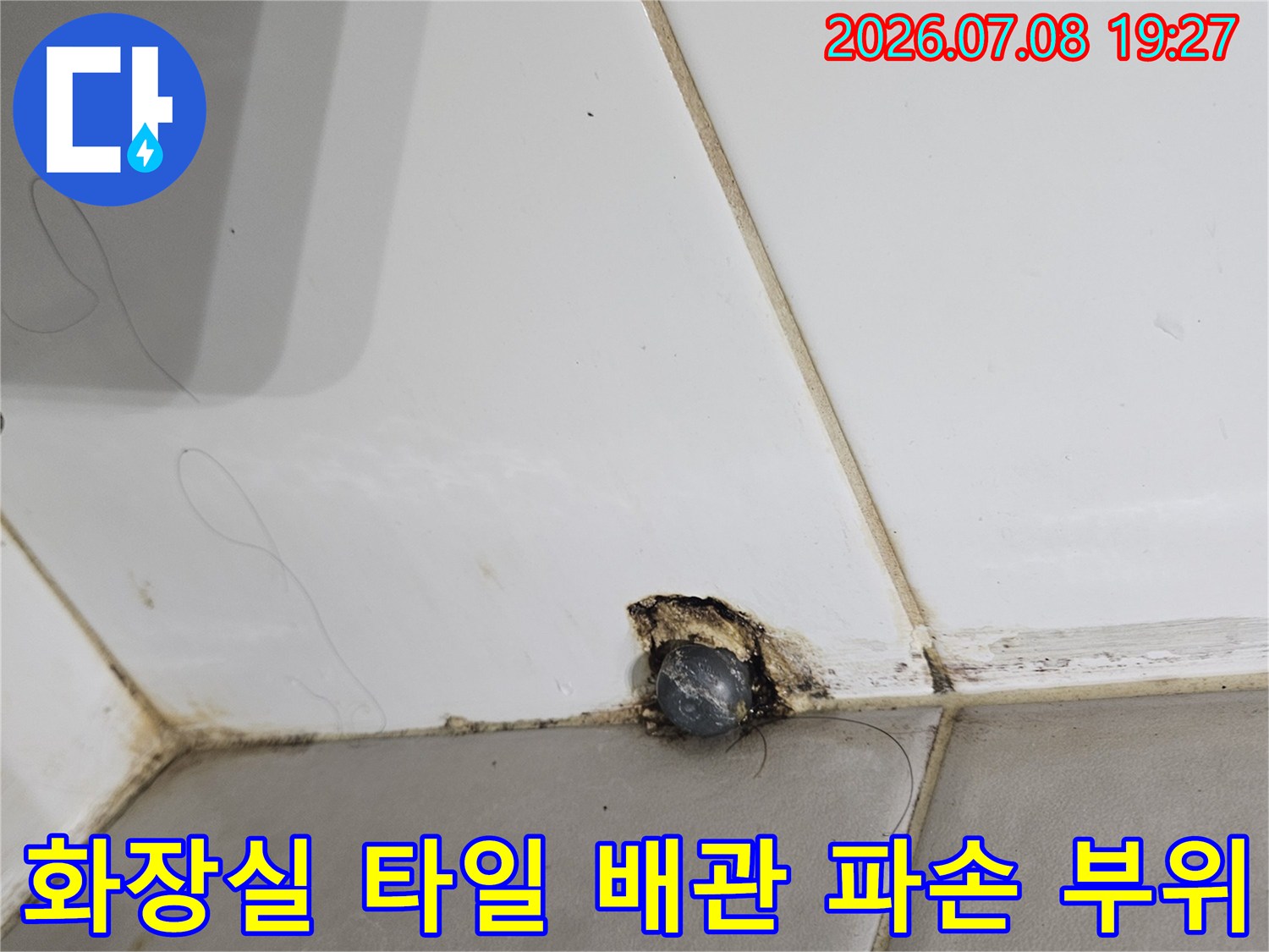 파손된 화장실 타일 사이로 노출된 배관 연결부와 주변 균열