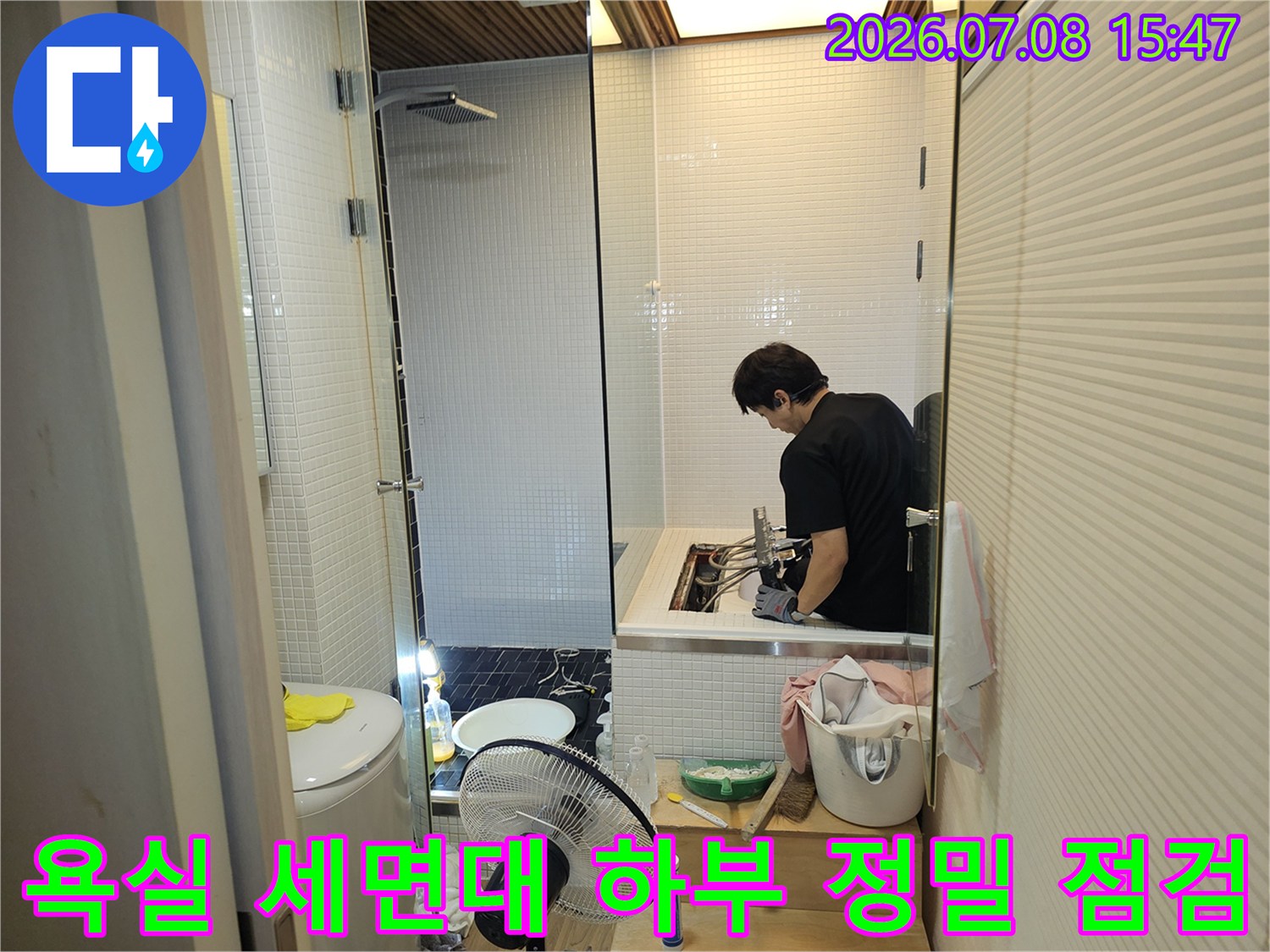 작업자가 화장실 바닥의 배출구와 세면대 아래 연결관을 상세히 검사하는 장면