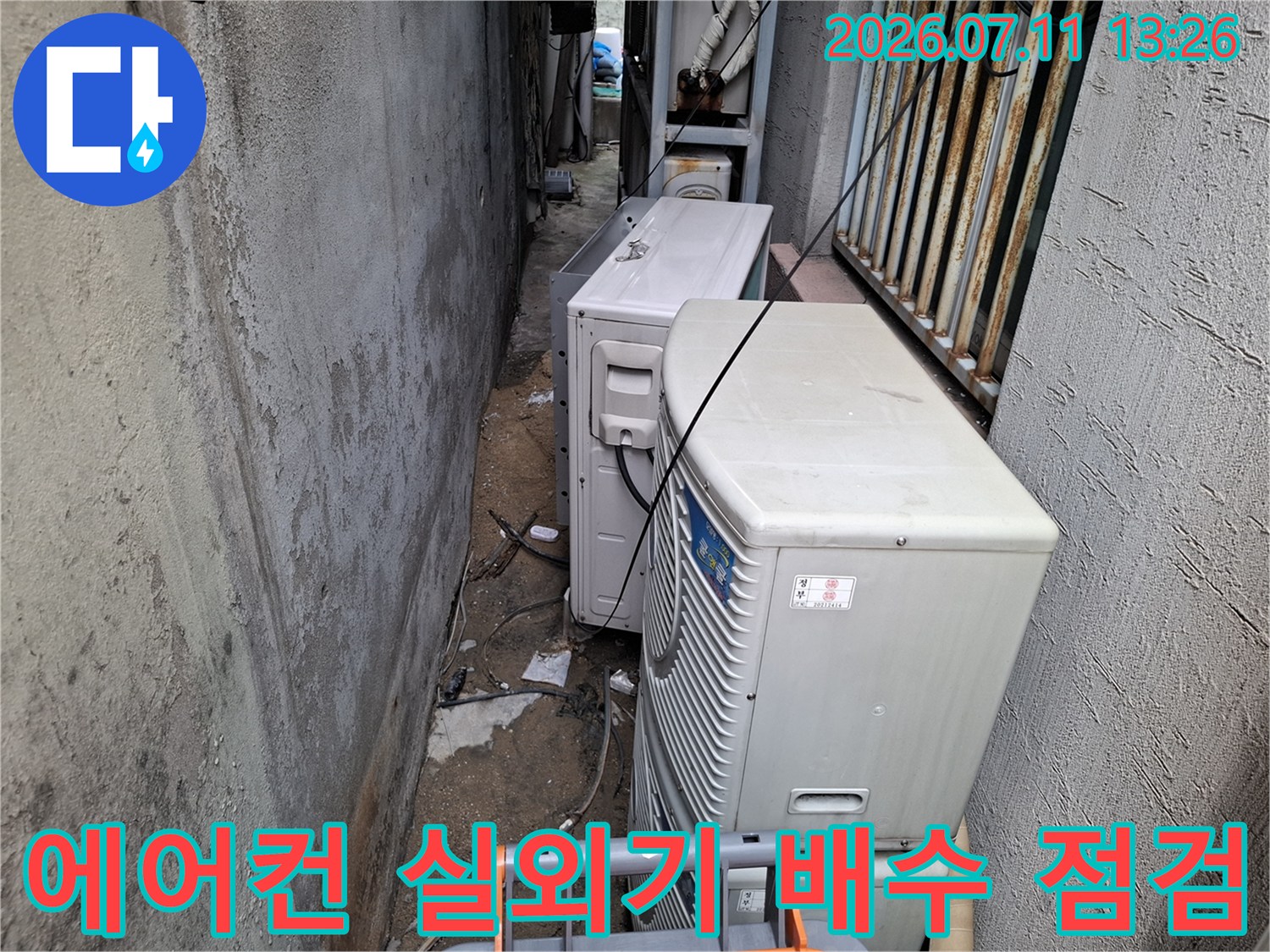 에어컨 실외기들이 밀집된 좁은 공간에서 드레인 배관을 점검하는 모습