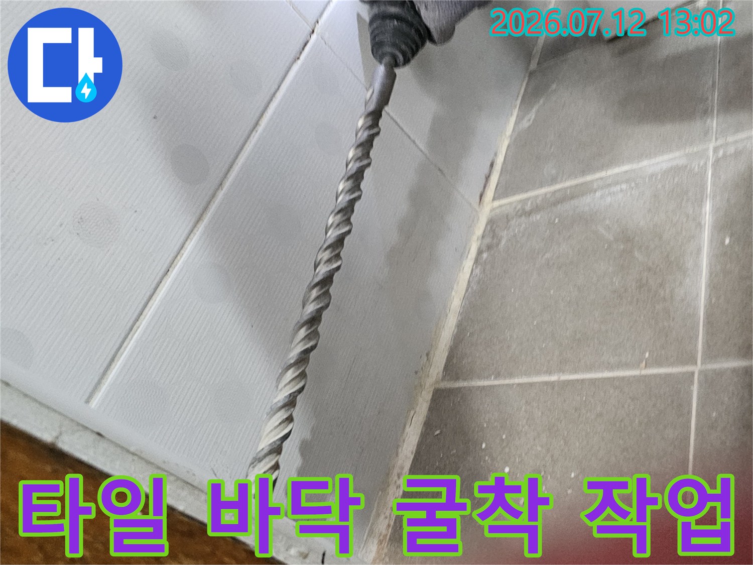 드릴 장비를 사용하여 타일과 시멘트 층을 제거하고 배관 노출 부위를 확보하는 장면