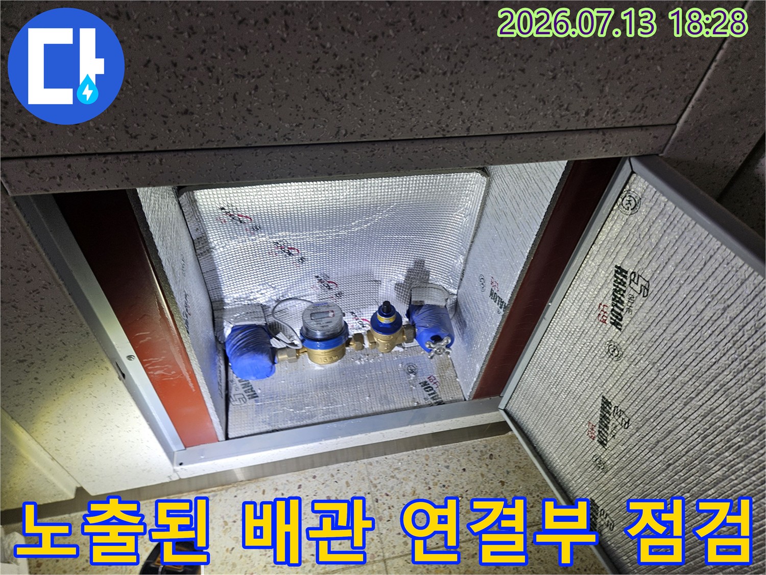 세탁실 바닥을 제거하고 노출된 수도 분배기와 배관 이음새를 검사하는 현장 사진