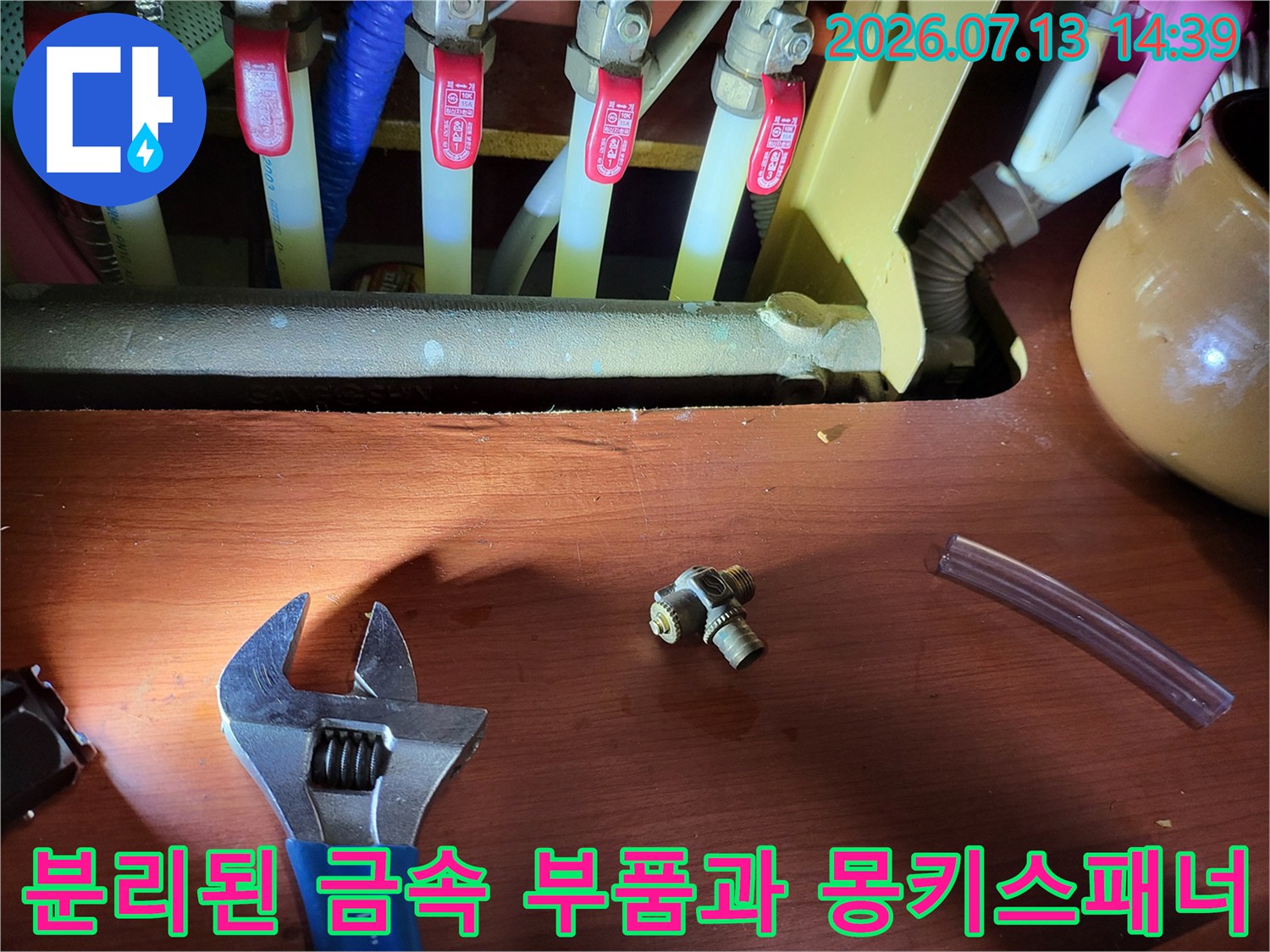 누수가 발생한 t자형 금속 연결재-투명 호스와 스패너가 함께 놓여 있는 모습
