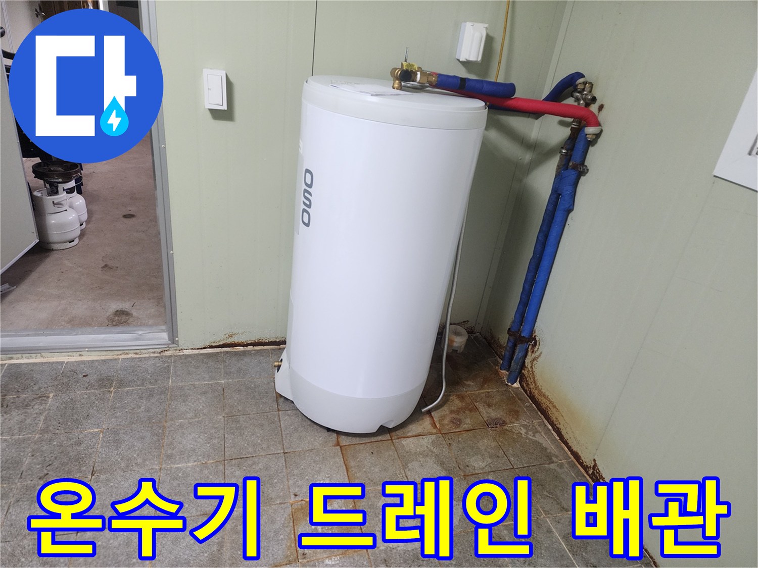 온수기 하단으로 연결된 파란색 배관과 타일 바닥 상태