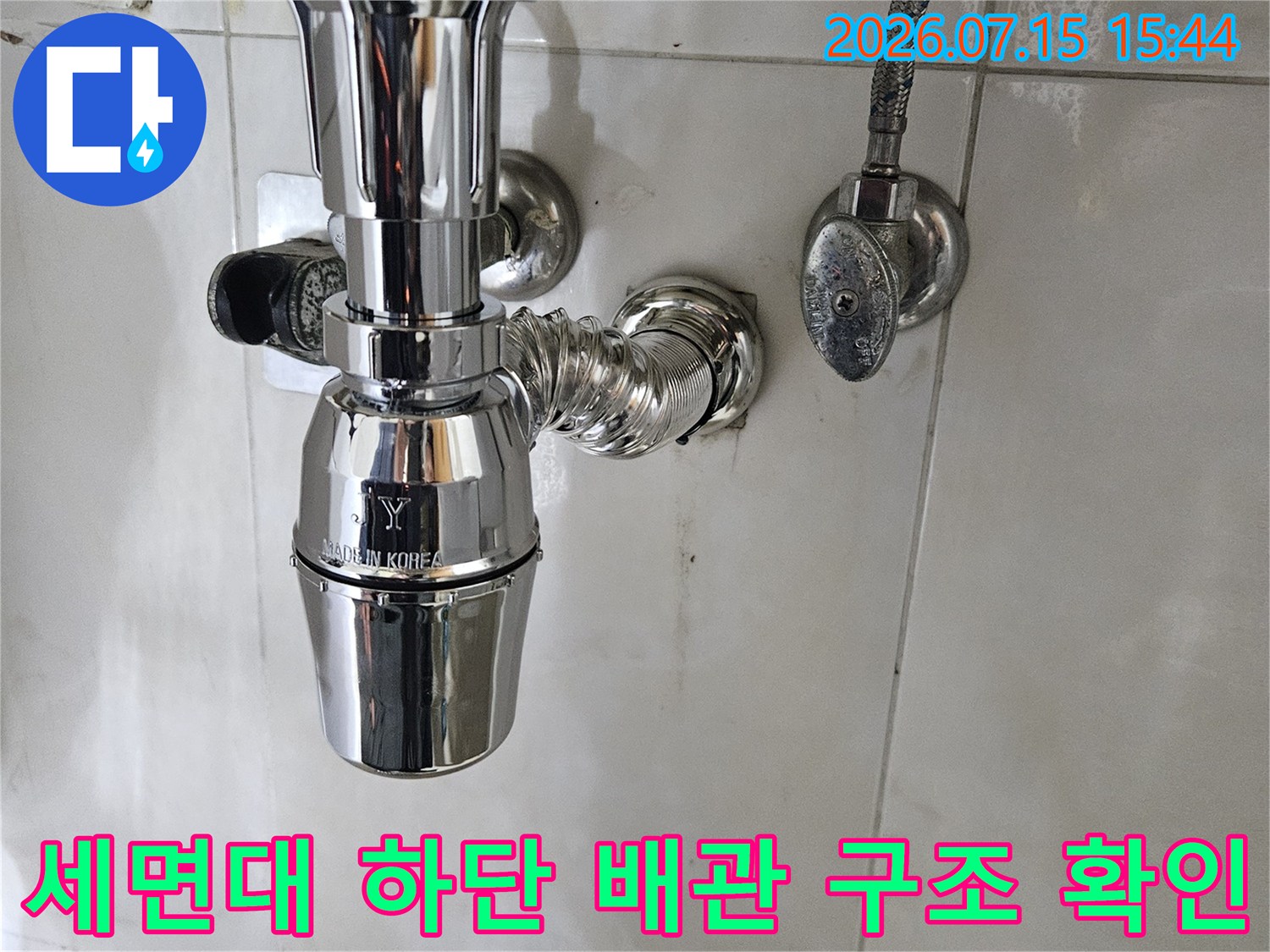 금속 재질의 세면대 연결용 배관이 설치된 욕실 내부 모습입니다.