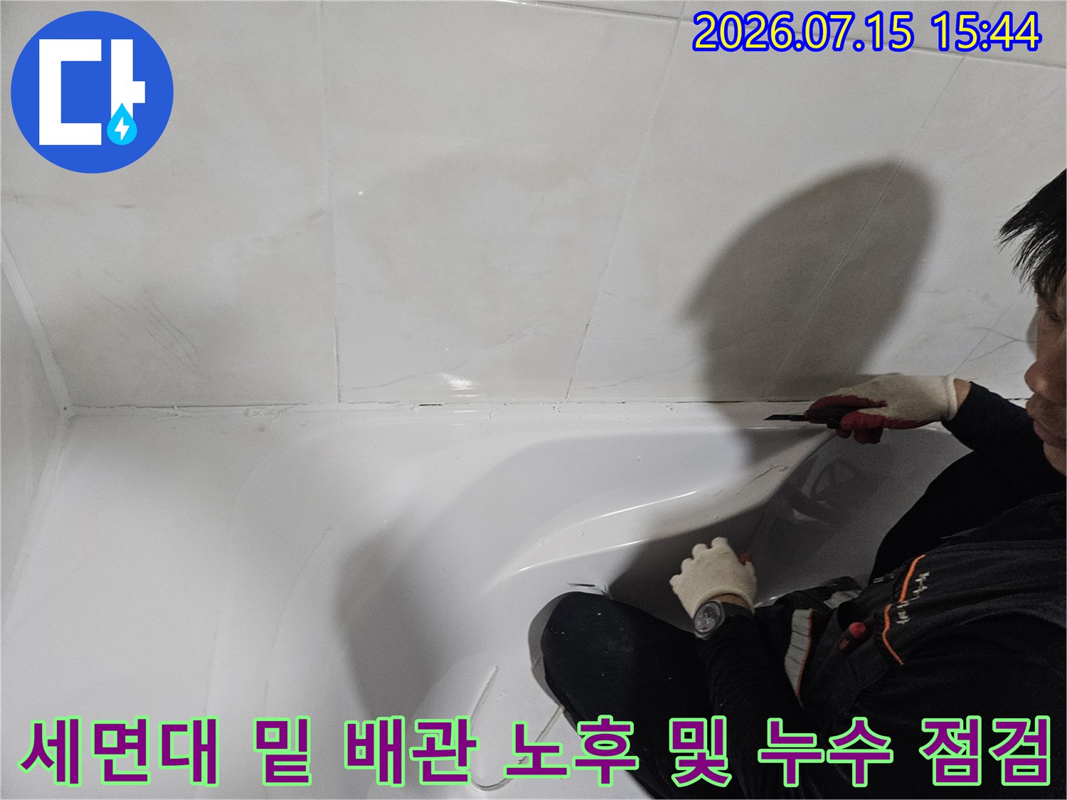 작업자가 장갑을 착용하고 세면대 하단 배관 연결부를 손으로 확인하는 장면