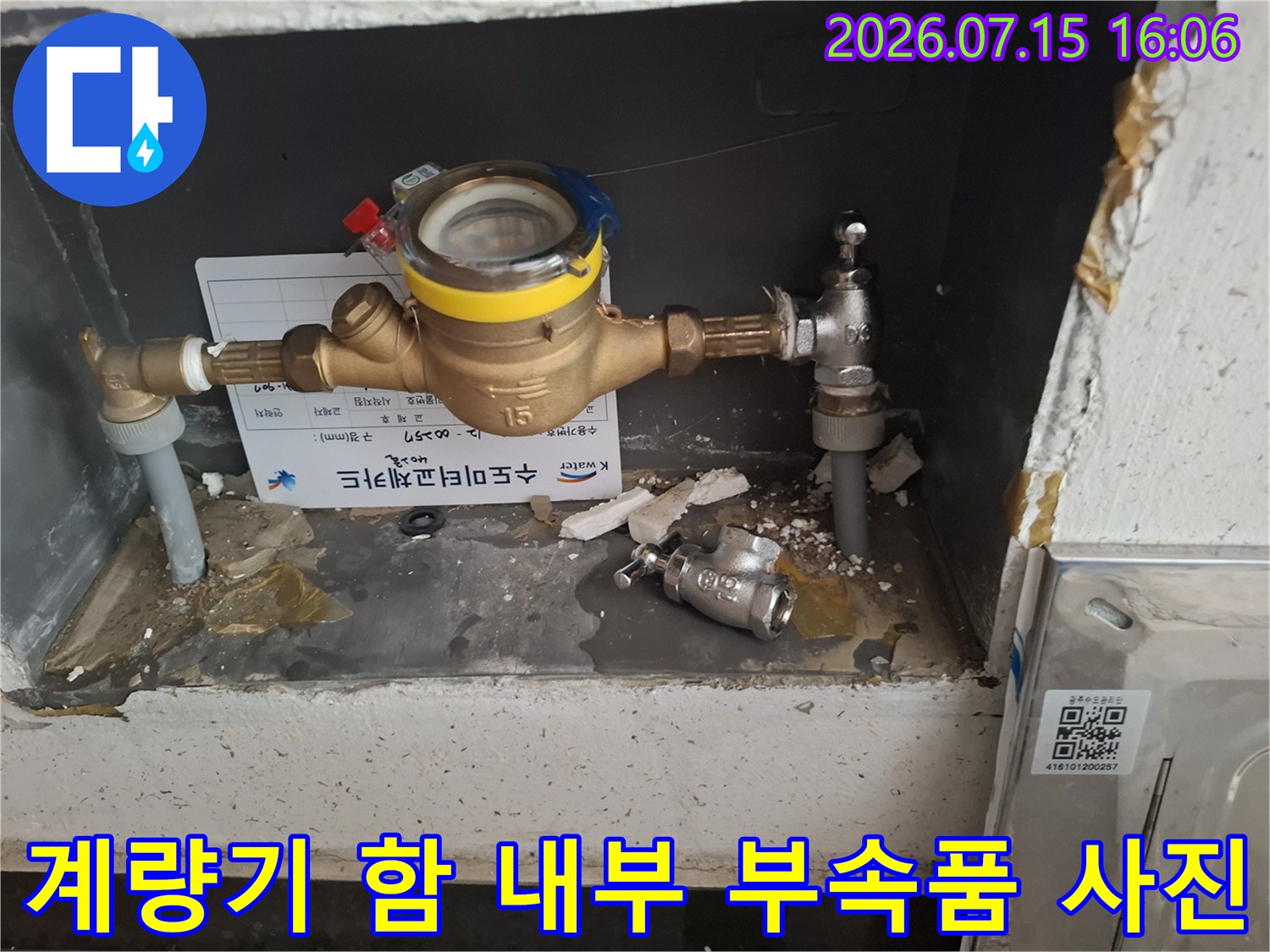 노란색 밴드가 둘러진 수도 계량기와 주변 배관-바닥의 잔해물들