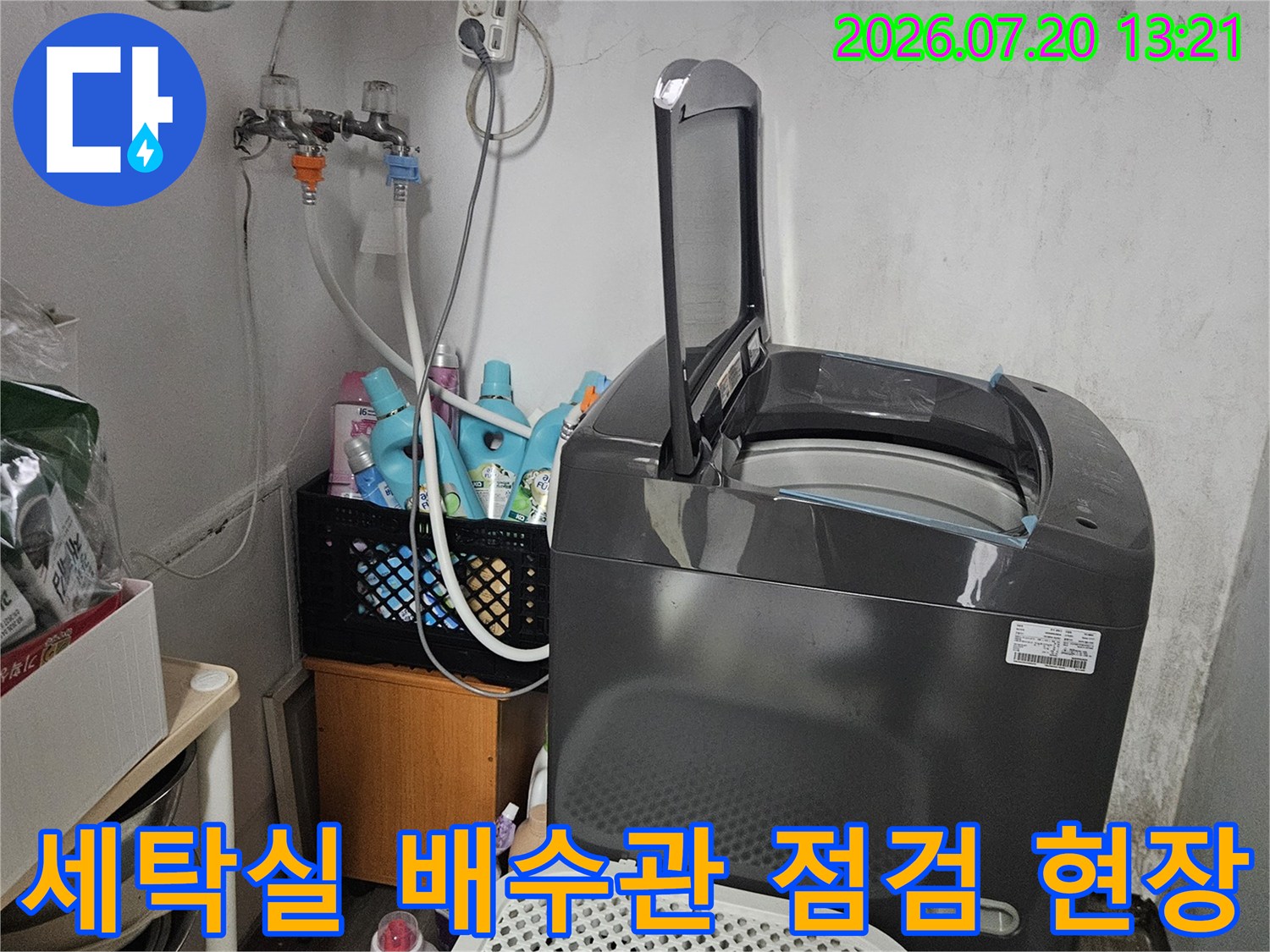 세탁기 옆에 위치한 회색 배수 파이프와 주변의 정리된 물품들이 보이는 세탁실 내부 전경