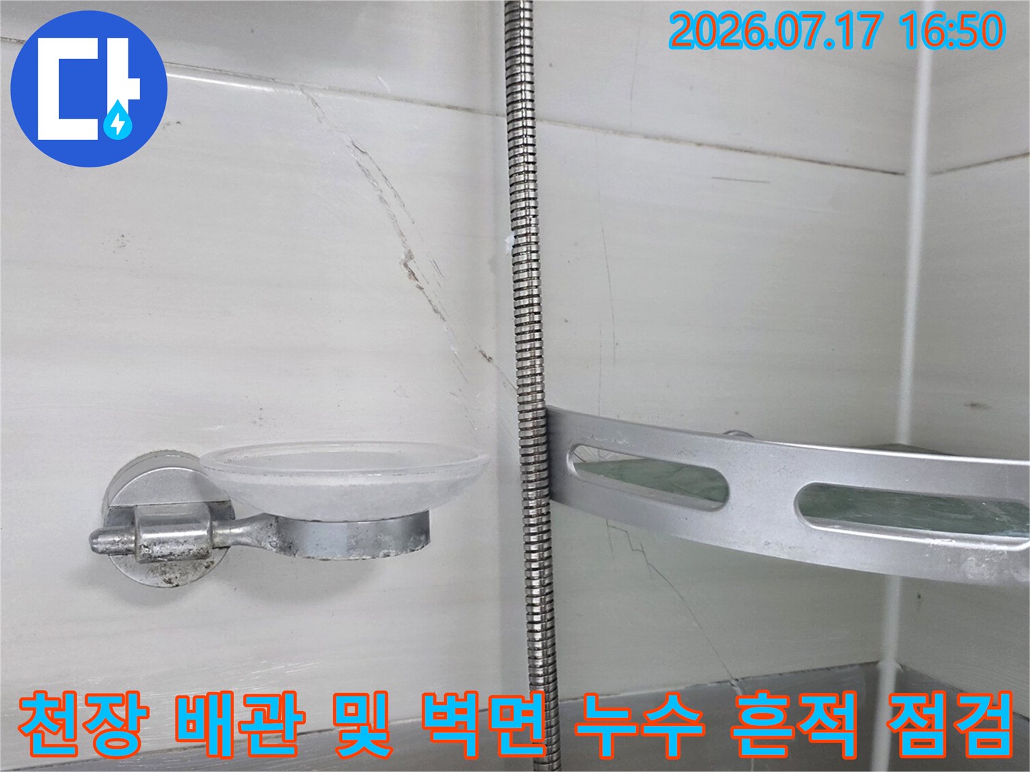 화장실 천장 내부의 노출된 금속 배관과 주변 콘크리트 면을 정밀하게 조사하는 모습