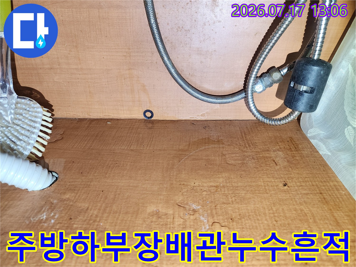 젖어서 색이 변한 나무 벽면과 그 앞에 설치된 금속제 배관-흰색 주름관 호스의 모습