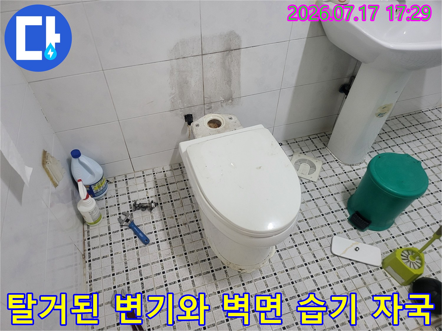 타일 바닥 위에-분리된 변기가 있고 뒤쪽 벽면에 짙은 누수 흔적이 남은 모습