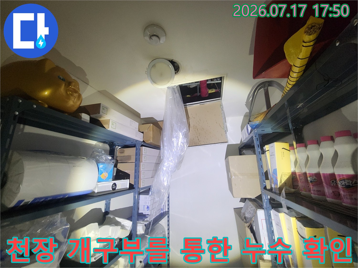 창고 천장의 열린 부분-상층 배관과 주변의 다양한 적재 물품들