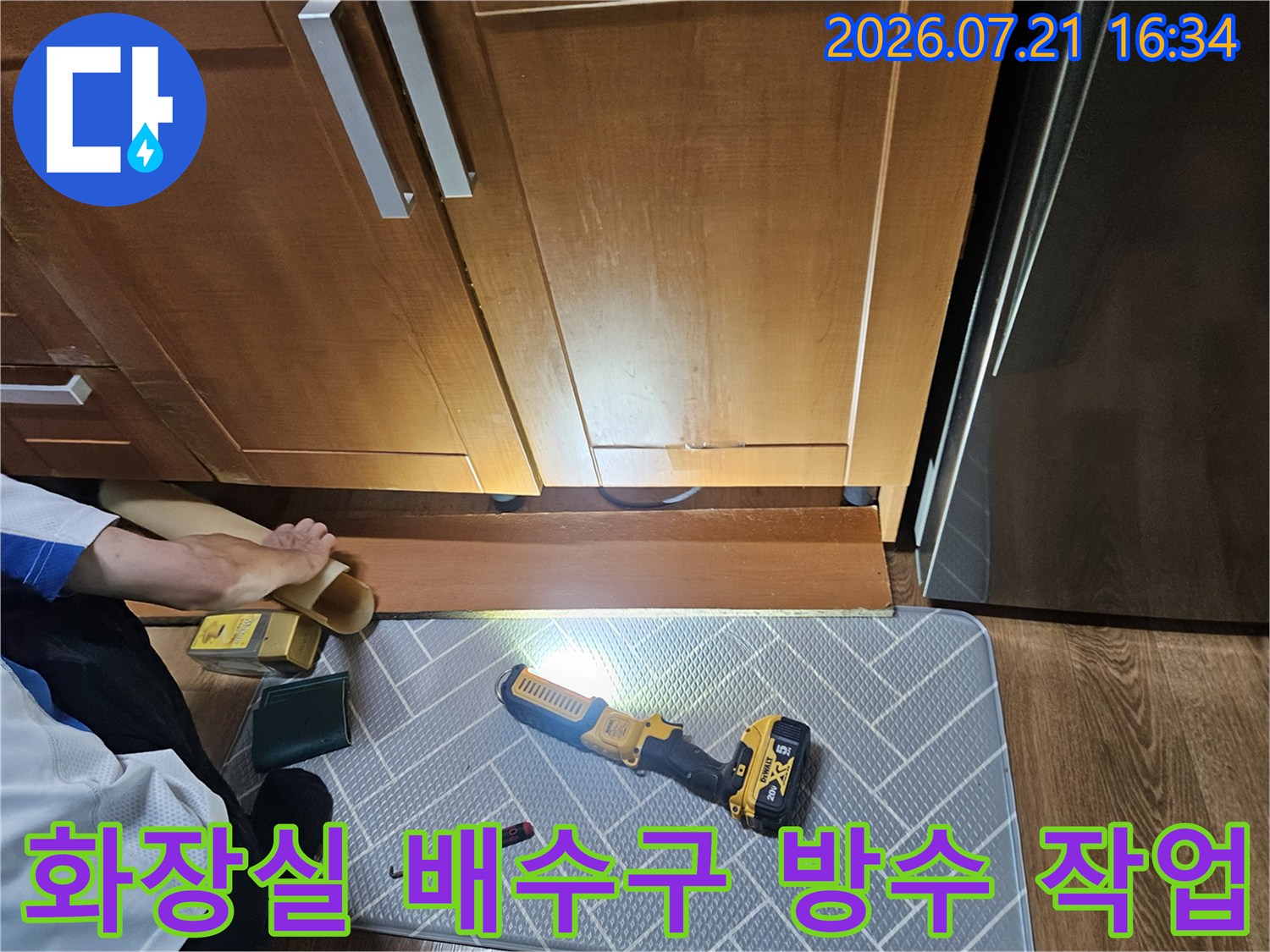 노란색 조명 아래 점검 중인 화장실 하부 배수구와 목재 수납장