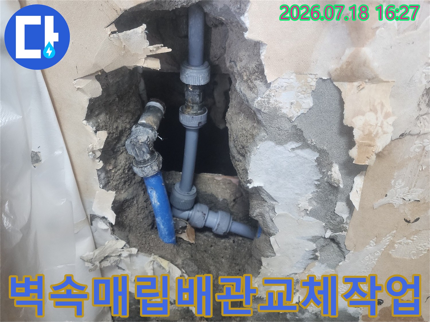 회색 벽면을 뚫어 드러낸 파란색 수도 배관의 수선된 연결 부위-주변 잔해물