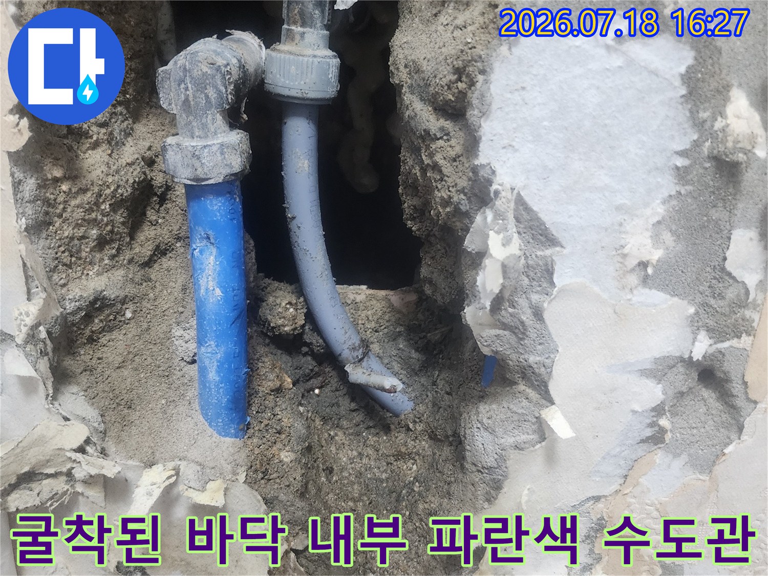 회색 콘크리트 잔해 사이로 드러난 L자형 연결 부속과 파란색 수도 배관-수선 전 모습
