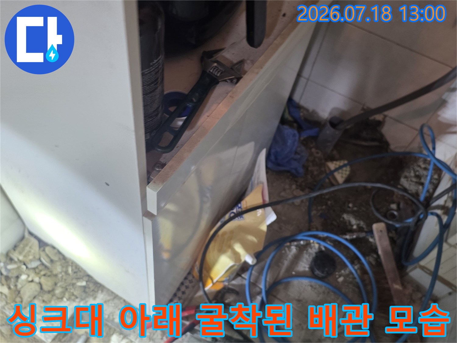 주방 싱크대 밑바닥이 파헤쳐져 있고 파란색 배관과 빨간색 집게 등이 놓인 현장 사진
