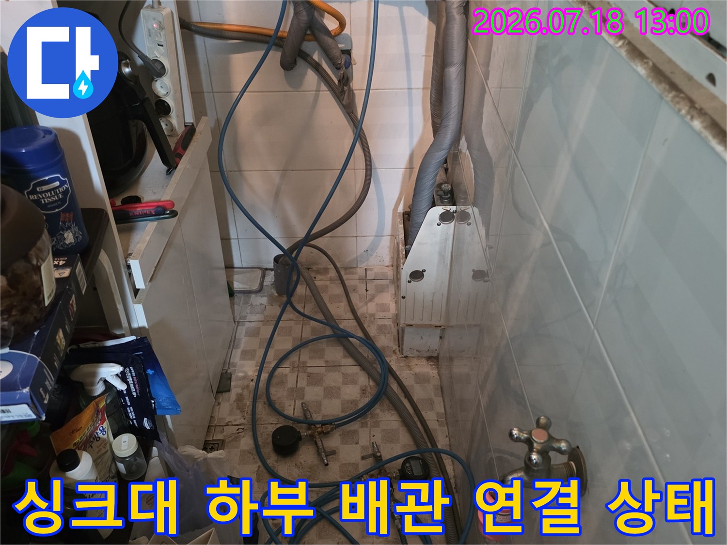 흰색 타일 벽면에 설치된 수도 밸브와 여러 갈래의 파란색 호스들이 배치된 모습