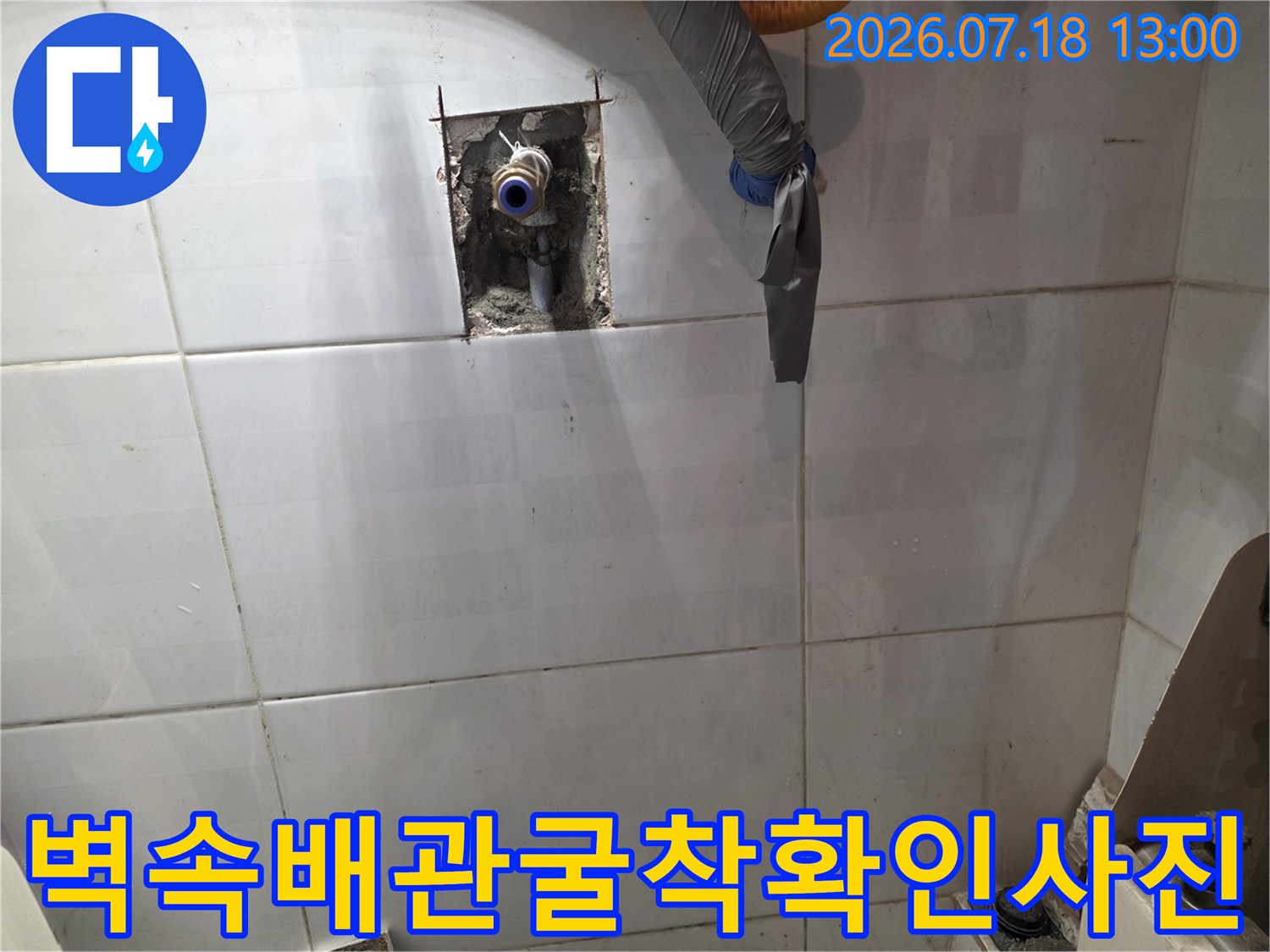 흰색 타일 벽면에 작은 구멍을 내어 매립된 파란색 수도 배관의 연결부를 드러낸 모습