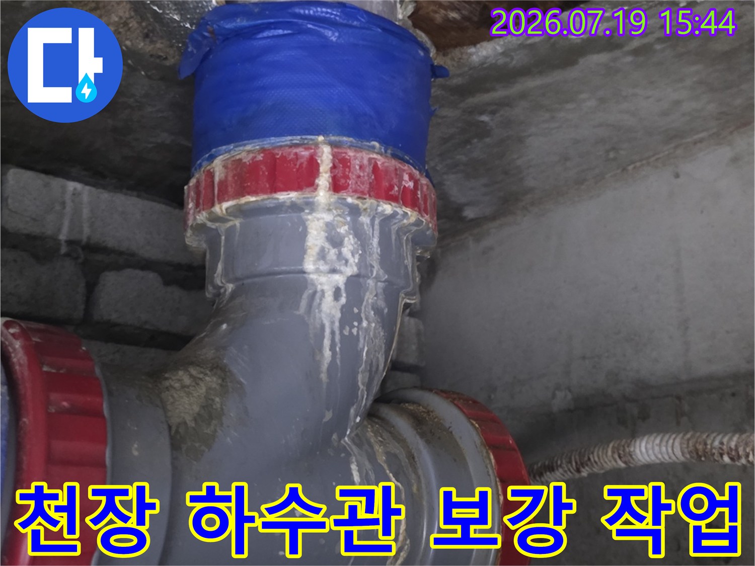 천장 콘크리트 틈새로 연결된 회색 PVC 배관의 접합부를 파란색 테이프로 감싼 모습