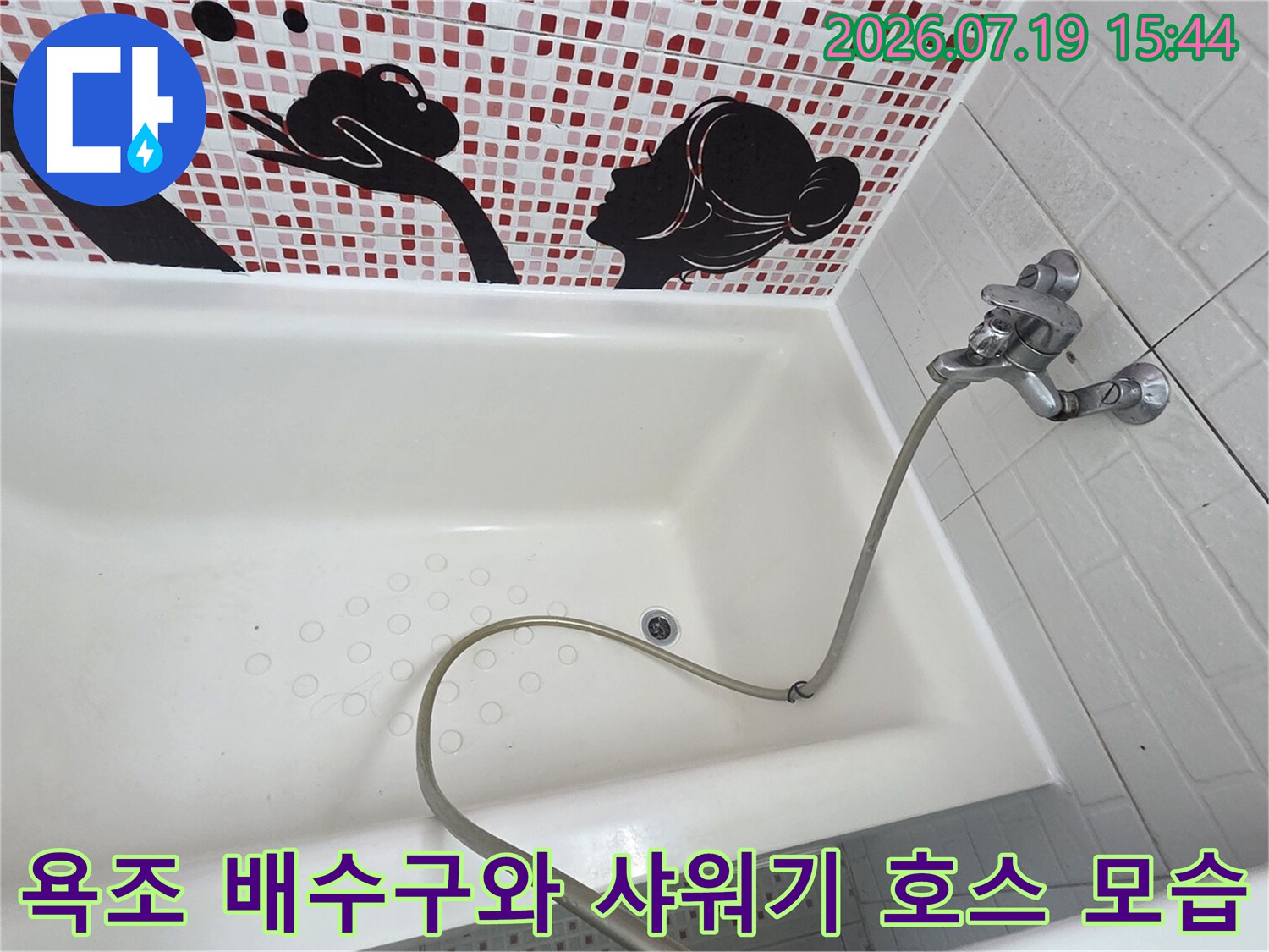 타일 벽면과 욕조가 이어진 지점에 수전이 설치되어 있고-바닥에 호스가 놓인 사진