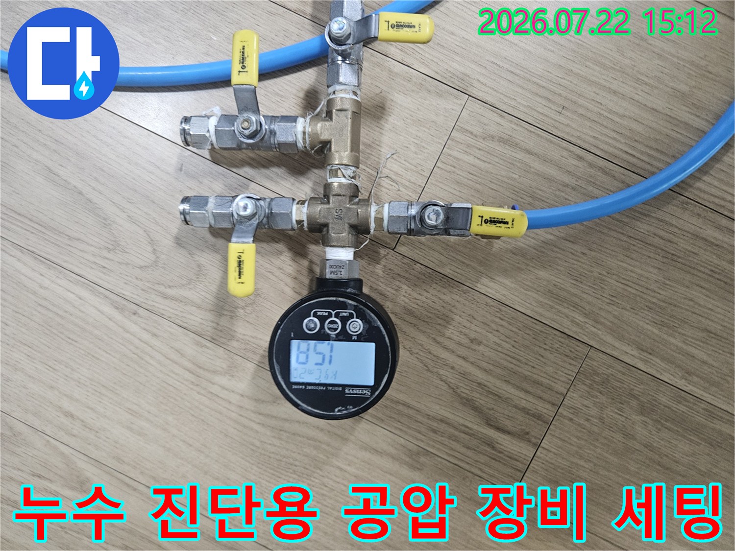 금속 밸브와 파란색 연결 호스가 복잡하게 구성된 배관 상단에 디지털 측정기가 부착된 사진