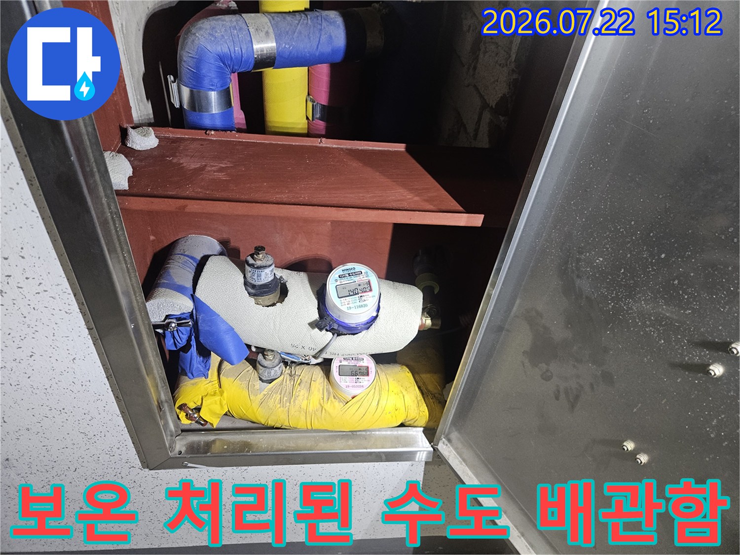 금속제 외함 속에 파란색과 노란색 단열재로 마감된 배관과 디지털 계량기가 설치된 장면