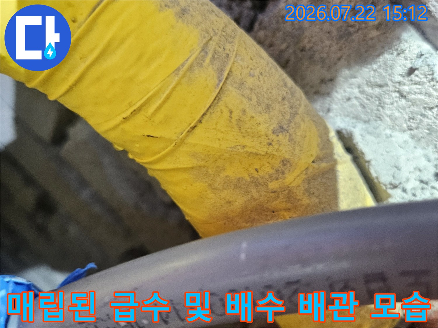 노란색 보온재가 감싸진-굵은 배관과 얇은 검은색 배관이 교차하는 천장 내부 모습