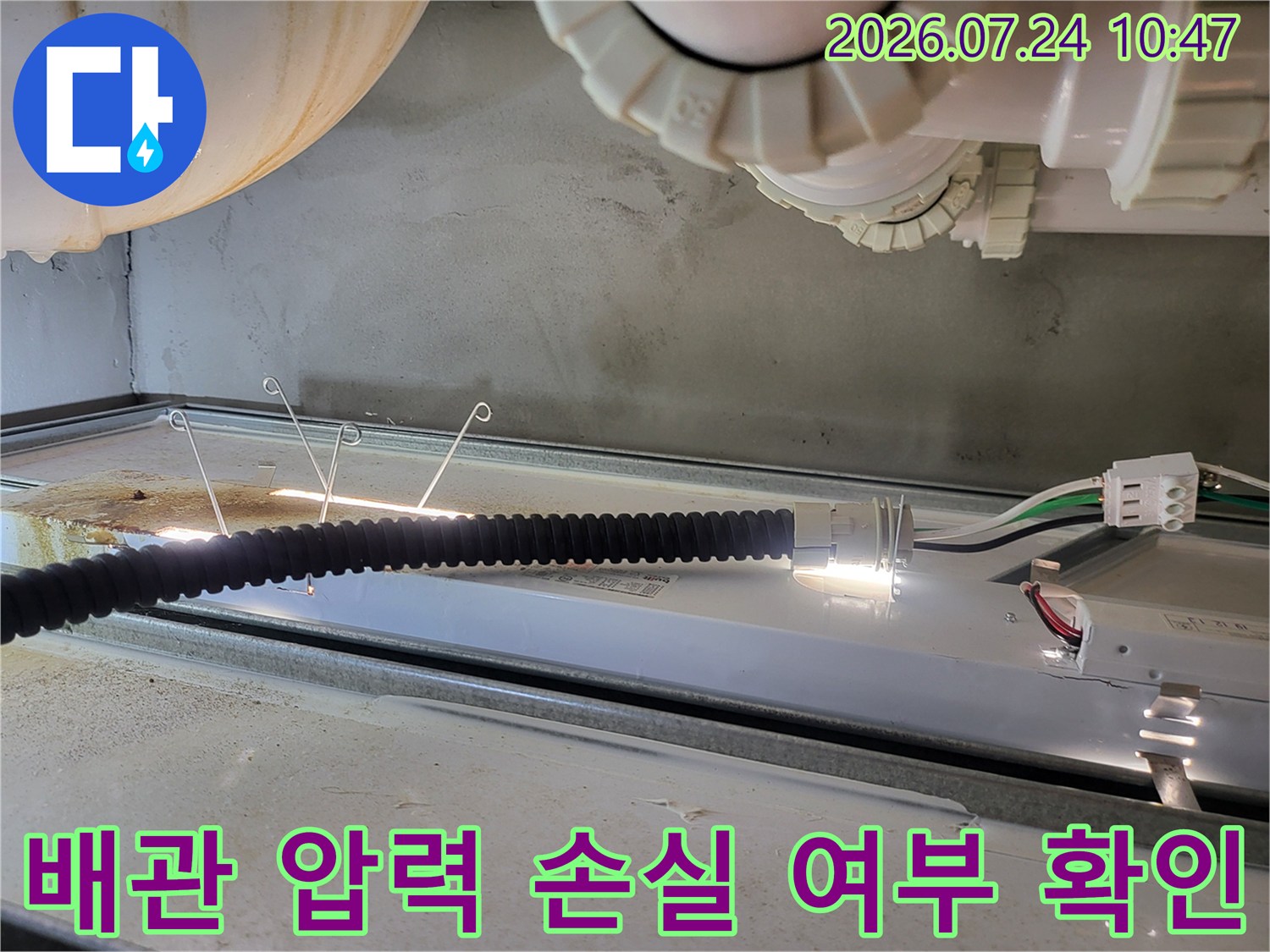 싱크대 하단 배관에 공압 시험 장비를 연결하여 누수 여부를 검사하는 모습