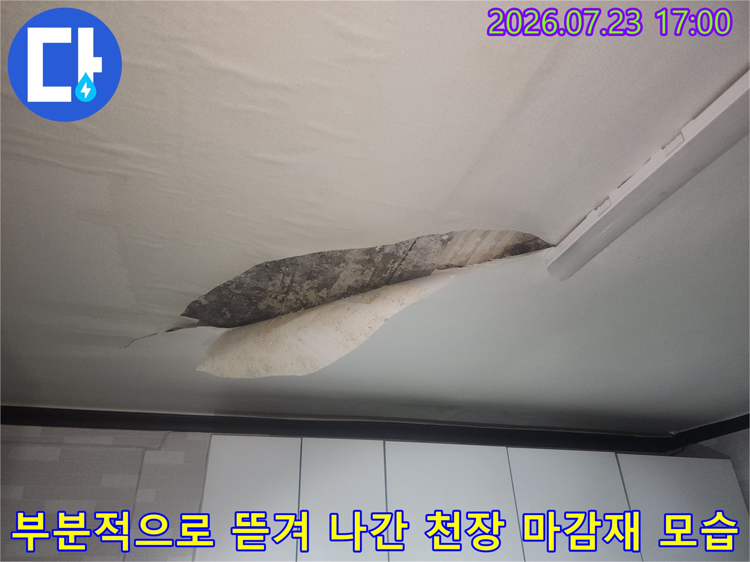 거실 천장의 흰색 마감재가 길쭉하게 파손되어 내부의 어두운 콘크리트 층이 노출된 상태