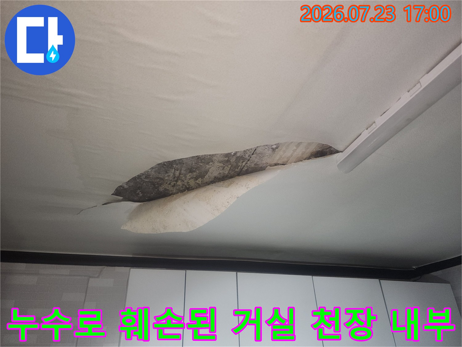 물에 젖어 찢어진 흰색 천장지와 그 너머로 보이는 어두운 색의 콘크리트 표면