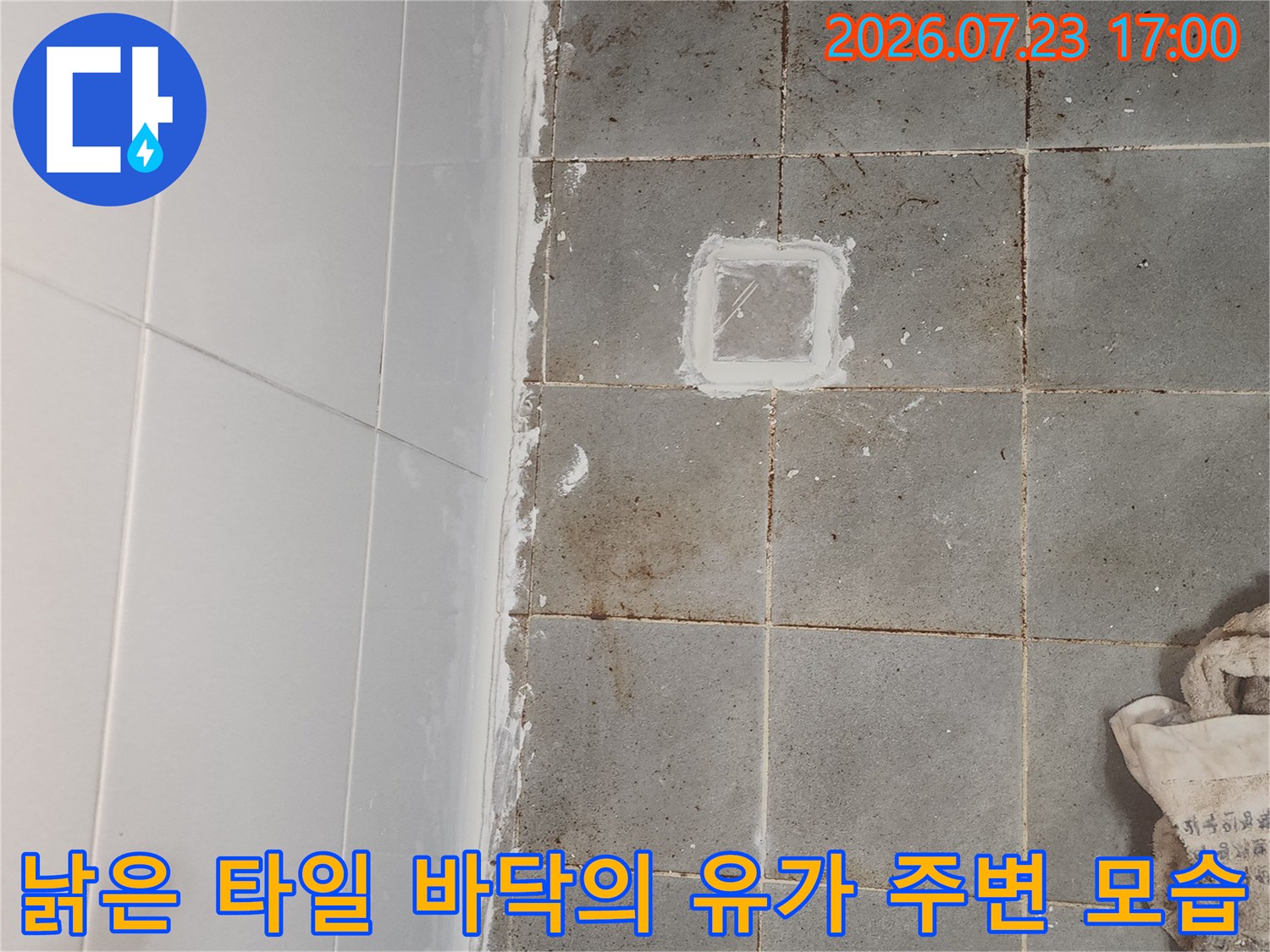 회색 욕실 타일 중앙에 위치한 사각형 모양의 배수구와 그 주변의 하얀 방수 자국