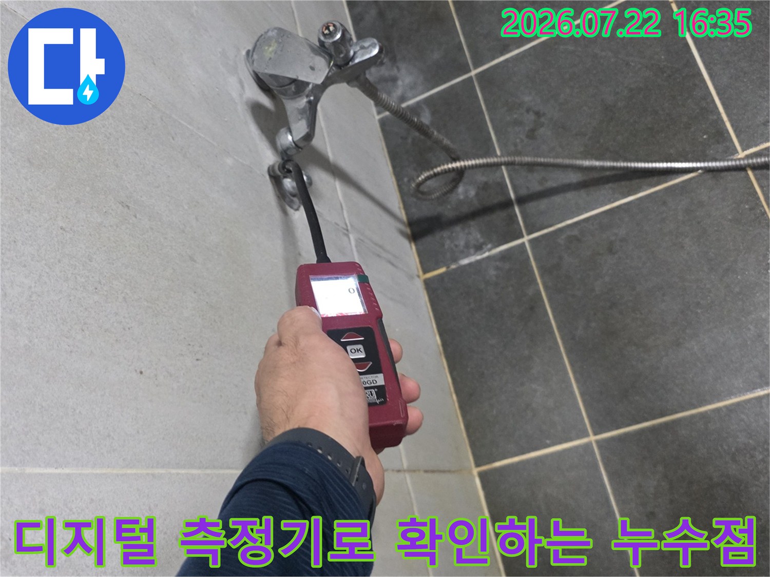 누수 탐지 엔지니어가-빨간색 휴대용 장비를 이용해-타일 벽면의-배관 연결부-이상 유무를 점검하는 장면