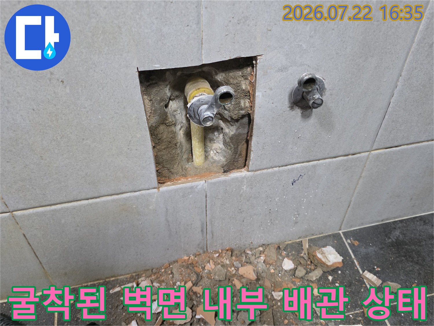 벽 타일을 굴착하여 매립되어 있던 노란색 수도 배관과 금속 밸브가 드러난 모습입니다