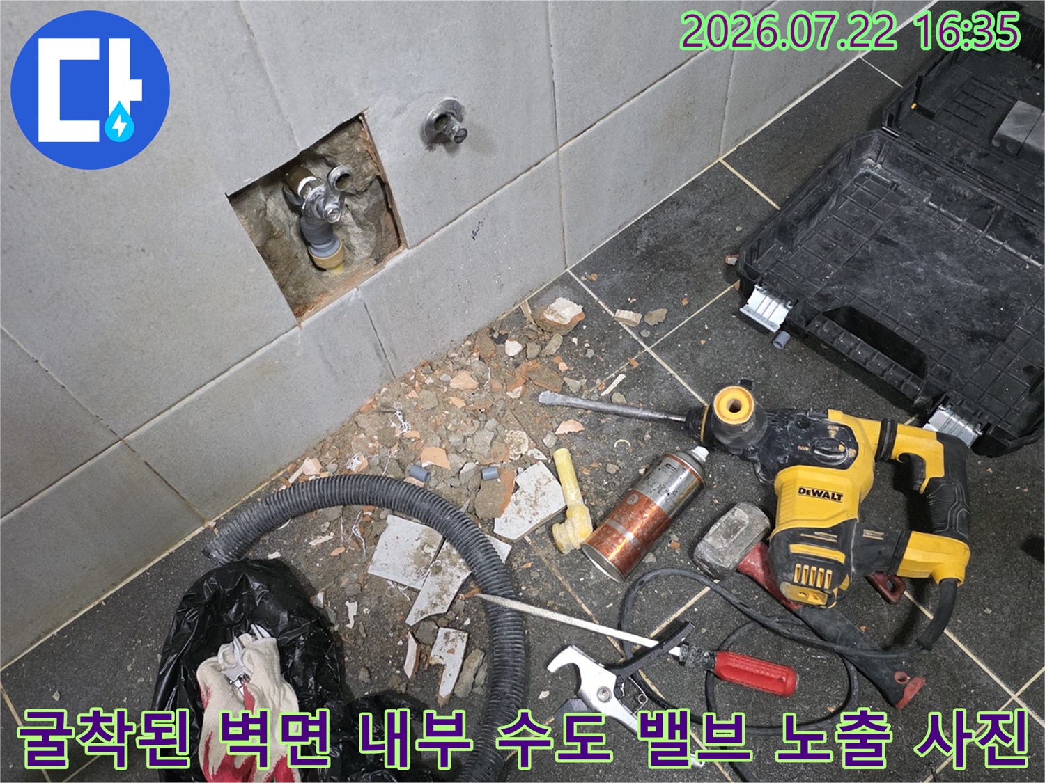 회색 타일 벽의 일부를 파내어 내부 금속 배관과 밸브가 보이며 바닥에 작업 도구들이 놓여 있는 현장