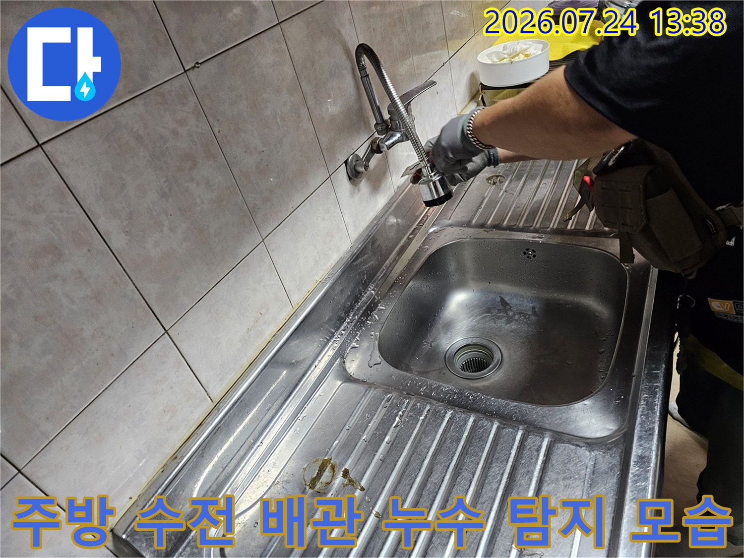 스테인리스 싱크대 볼 위로 설치된 수전의 연결 상태를 점검하는 작업자의 모습