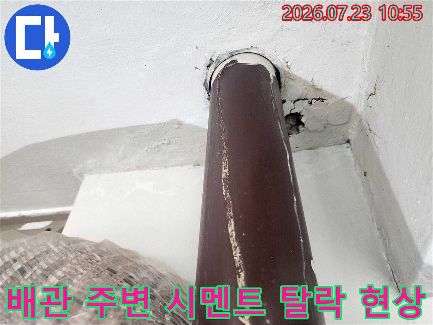 흰색 벽면과 갈색 온수 배관 사이의 접합부가 벌어져 균열이 생긴 모습