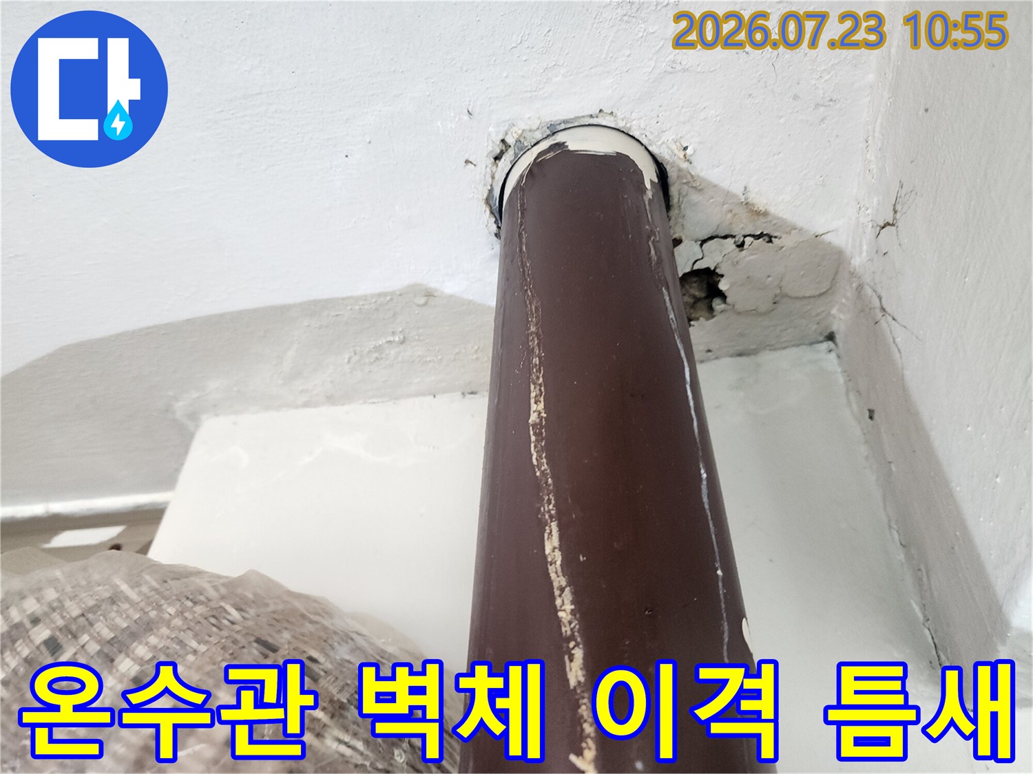 흰색 페인트 벽면과 갈색 배관 사이의 벌어진 틈과 주변 균열 모습