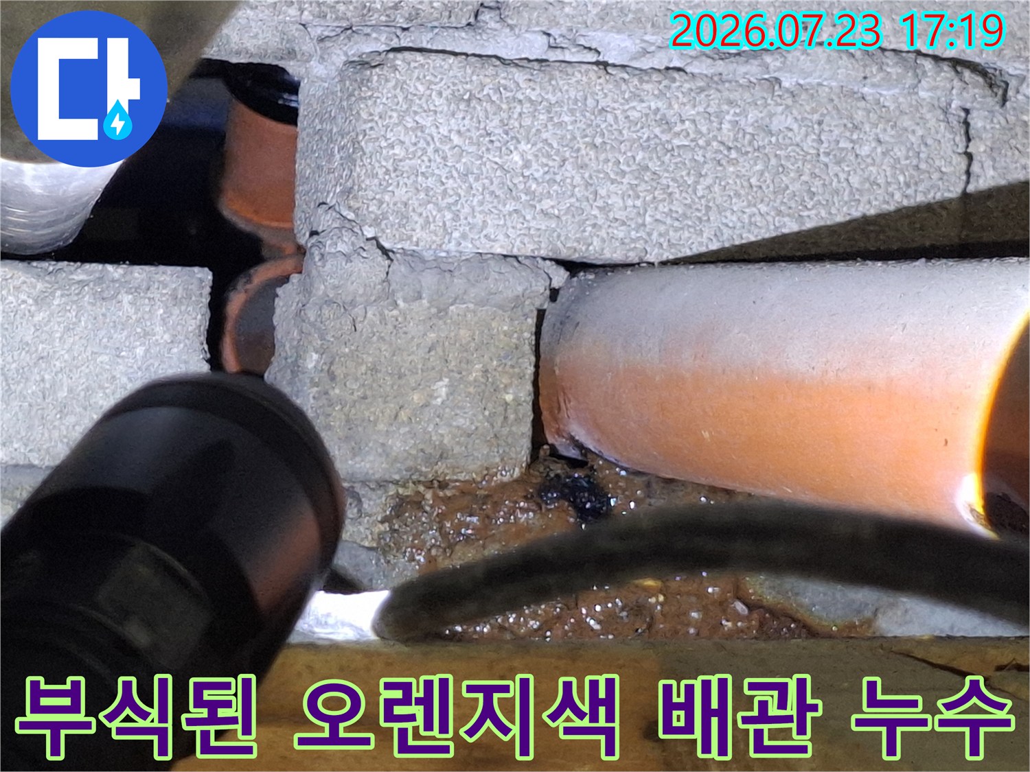 콘크리트 벽면 아래로 지나가는 부식된 오렌지색 배관-누수 지점 사진