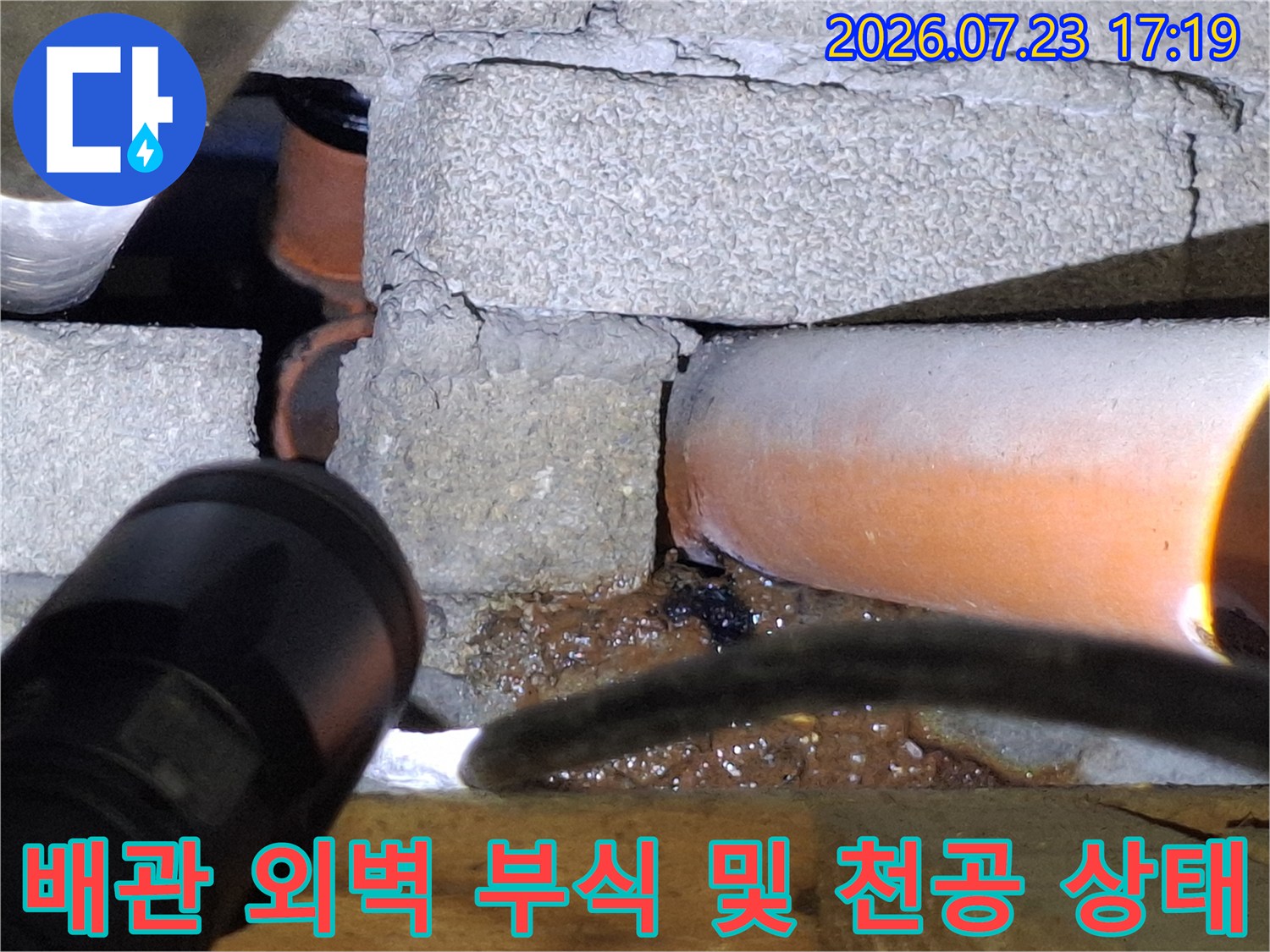 콘크리트 틈새에 매립된 오렌지색 배관의 파손 부위를 비추고 있는 사진