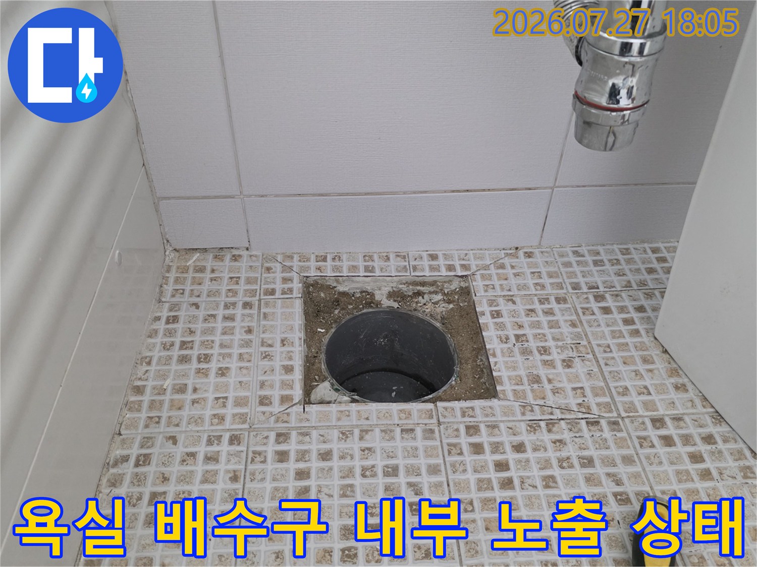화장실 바닥의 기존 유가 덮개가 제거되어 내부 배수관과 주변 시멘트 층이 드러난 모습