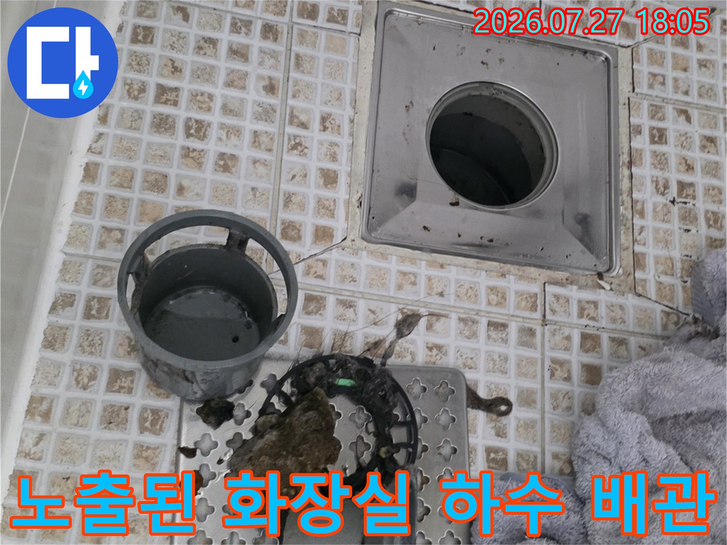 흰색 타일 바닥에 설치된 정사각형 배수구와 옆으로 치워진 트랩 부속들