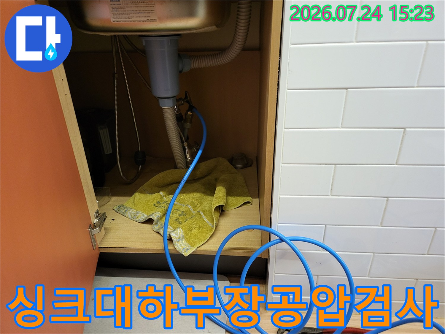 싱크대 하단 배관에 파란색 공압 테스트 호스를 연결하여 누수를 점검하는 모습