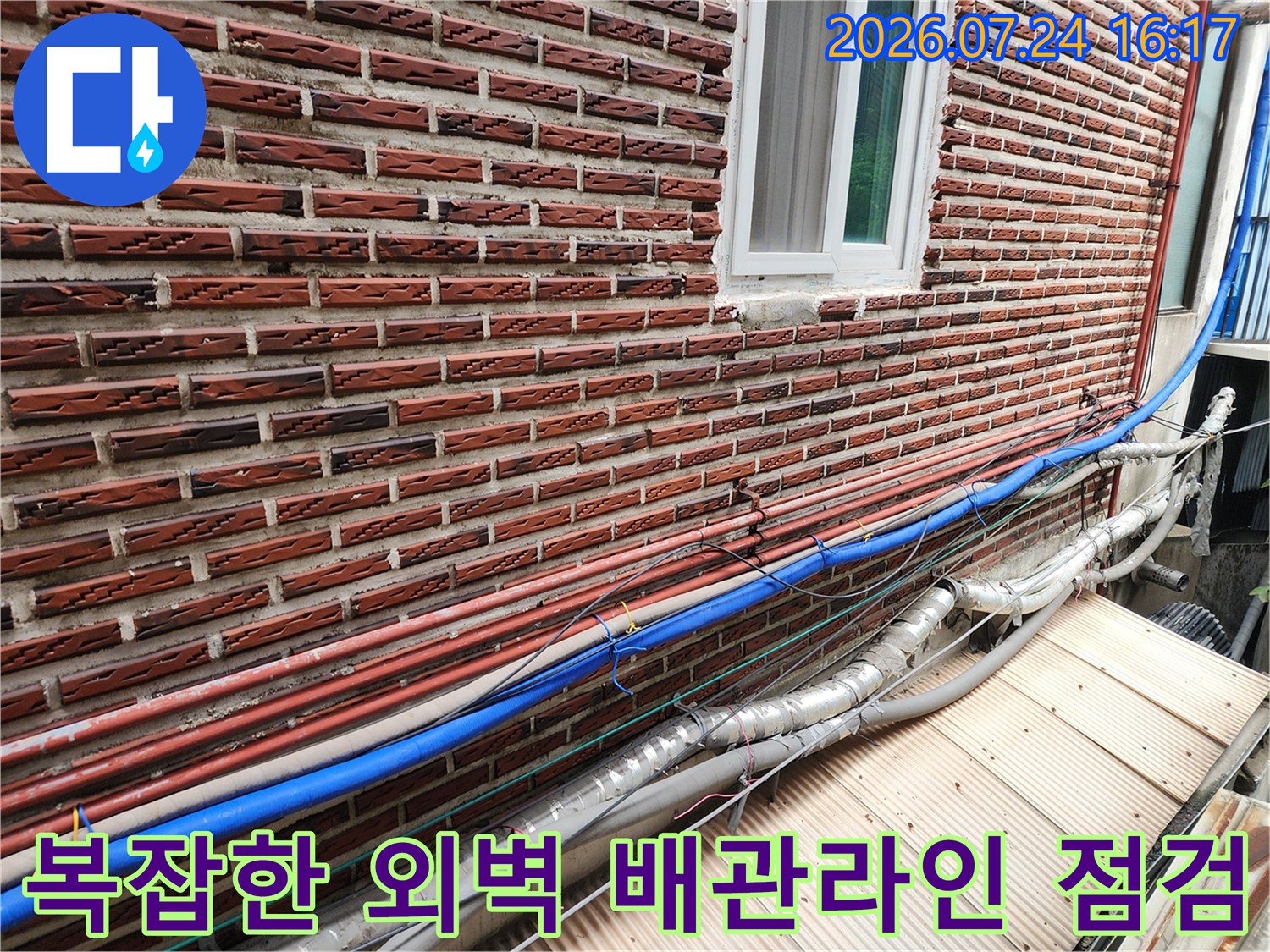 벽돌 벽체에 고정된 파란색과 은색 단열재 마감의 다중 수도 배관들