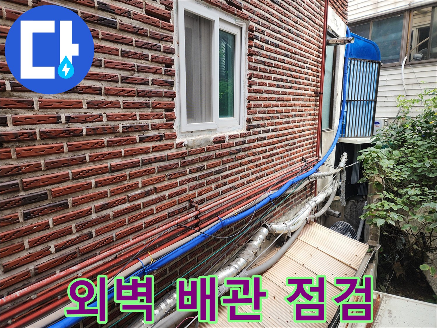 붉은 벽돌 외벽에 설치된 파란색과 은색 보온재가 씌워진 노출 배관들