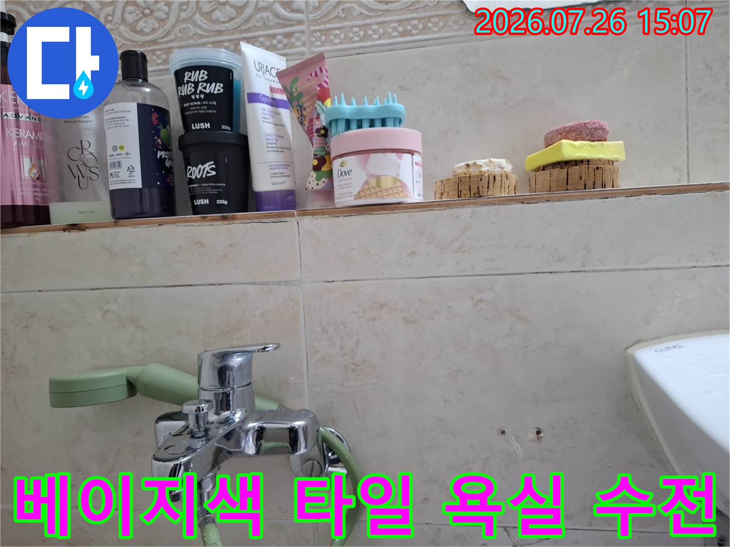 욕실 벽면에 부착된 금속 수전-샤워기 헤드 연결부와 주변의 베이지톤 타일 마감