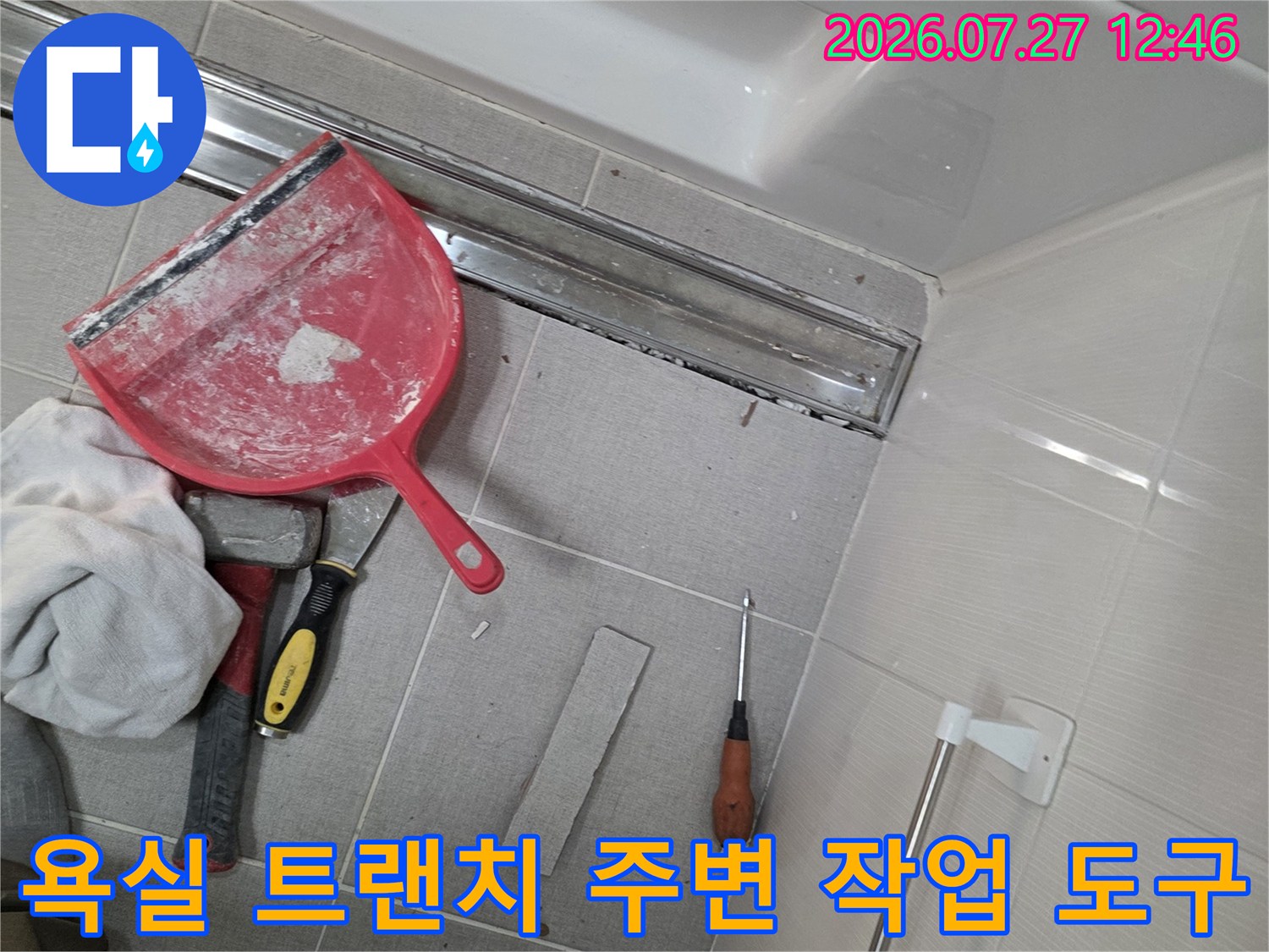 욕실 바닥의 금속제 트랜치-배수구와 그 주변에 놓인 빨간색 헤라 및 수공구들