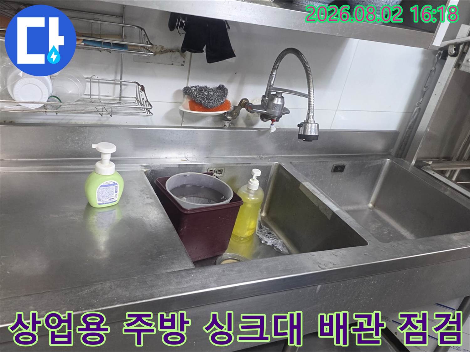 상업용 주방의 스테인리스 싱크대에 놓인 세제와 노출된 배관 구조