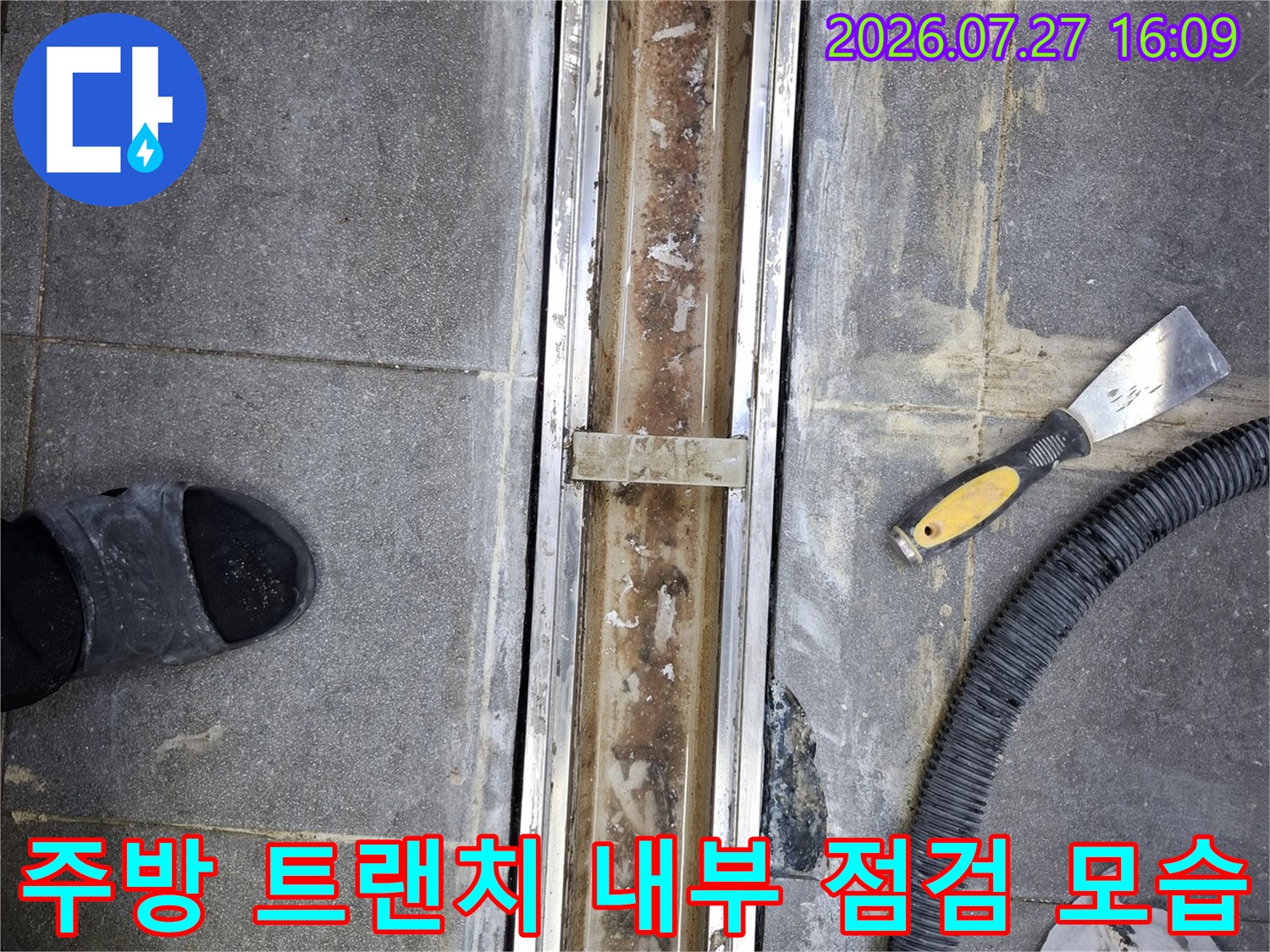 식당 주방 바닥의 스테인리스-트랜치 덮개가 열려 있고 주변에 작업 도구가 놓여 있는 모습