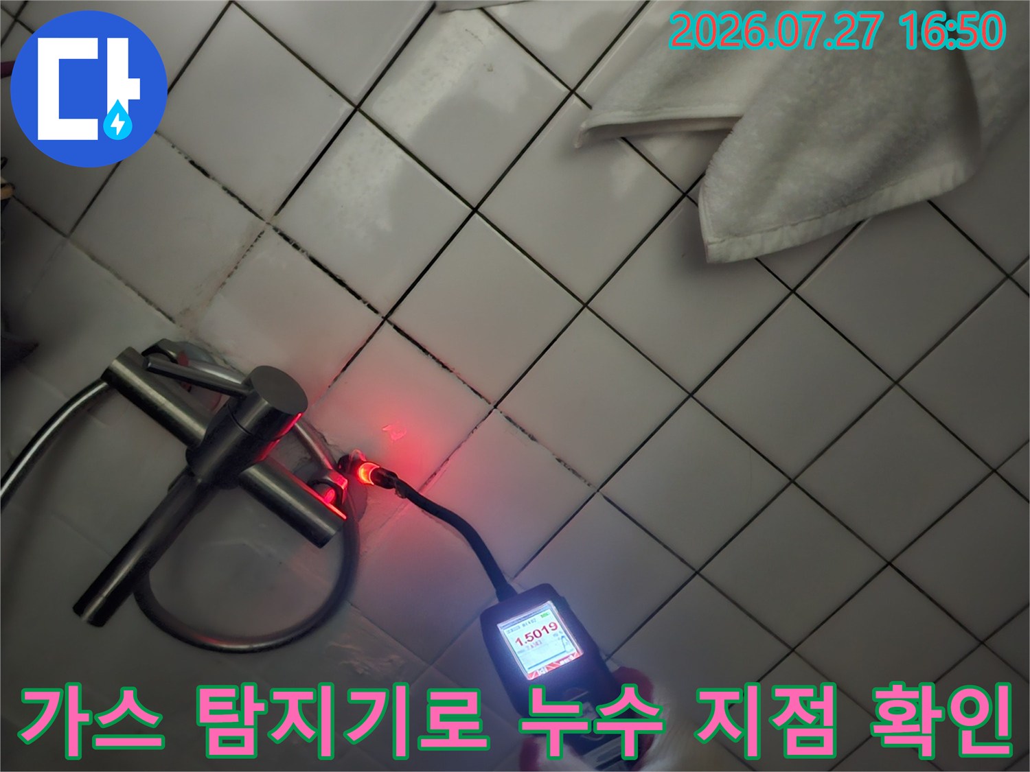 하얀색 타일 바닥의 배관 연결 부위에 가스 탐지기를 대고 수치를 측정하고 있는 모습